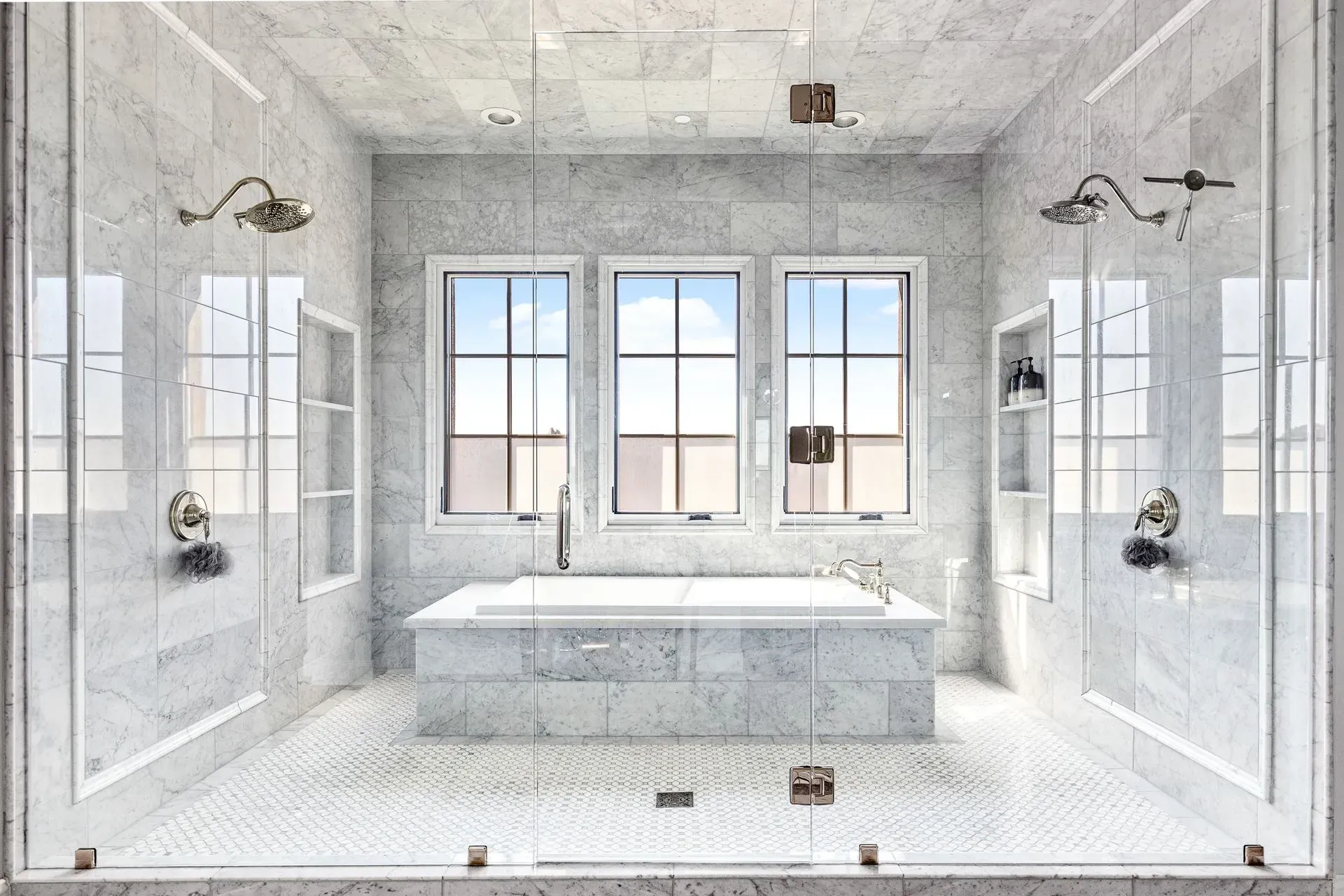 Luxurious bathroom with marble walls, a bathtub, glass shower doors, and three windows.