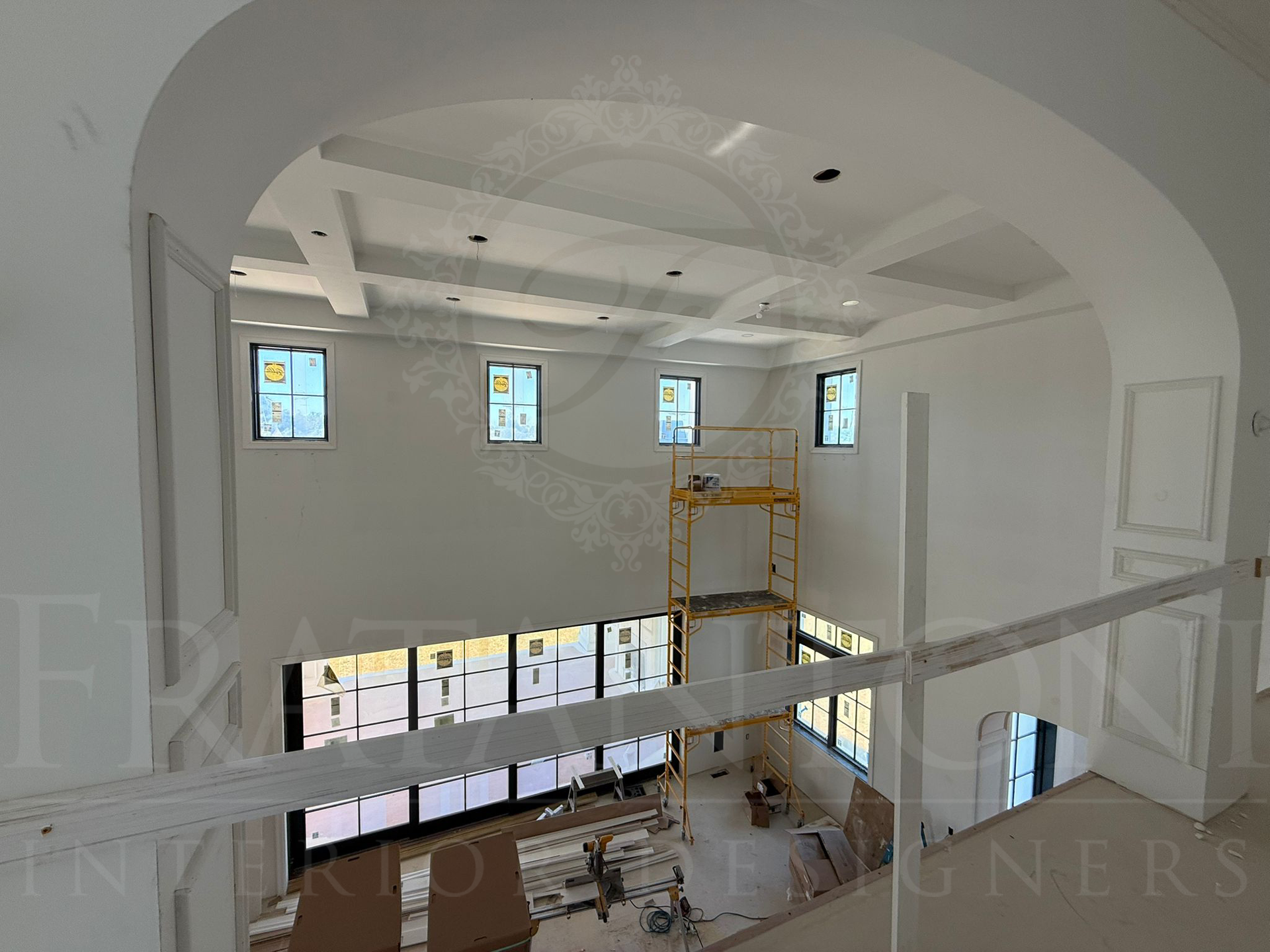 A high-ceilinged room under construction with a yellow scaffolding tower, large window grid, and white arched entryway.