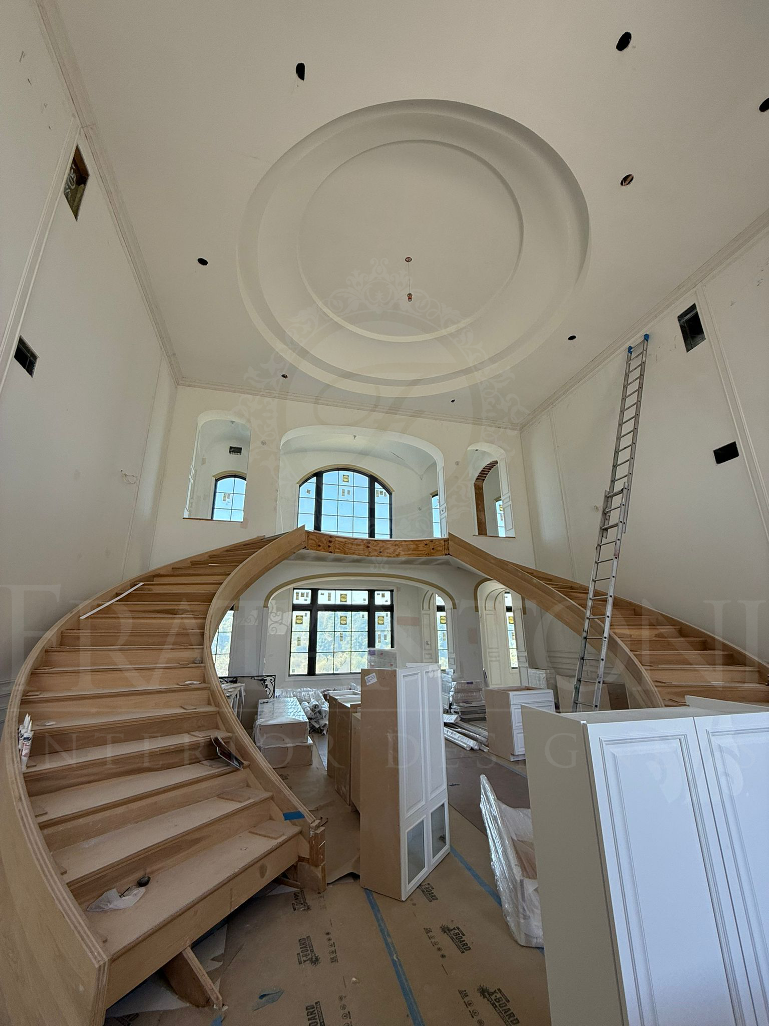 Grand staircase in an unfinished luxury foyer with ornate ceiling and large windows