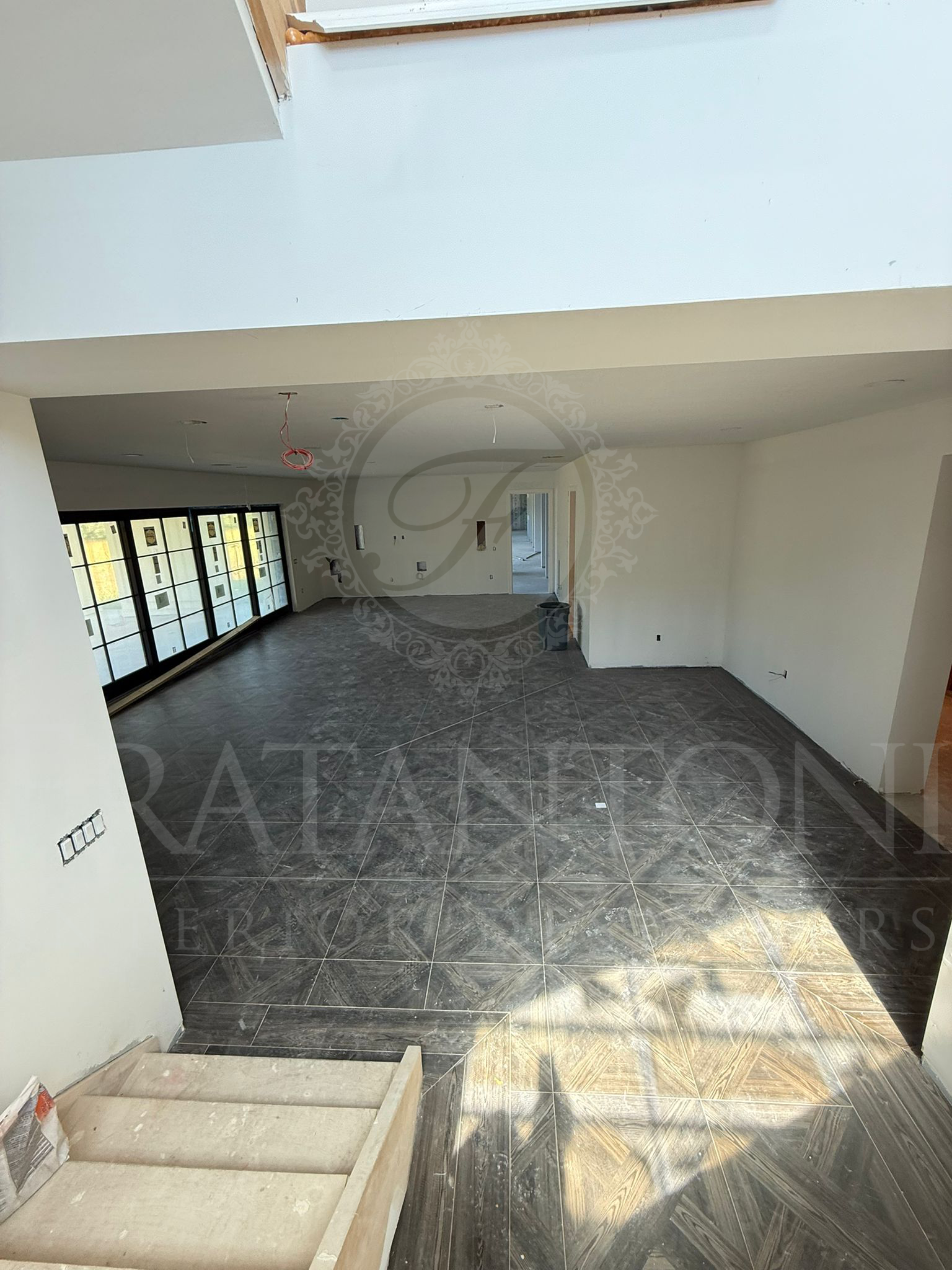 An elevated view of a spacious, open-concept living area with dark, mottled tile flooring and large windows on the left.