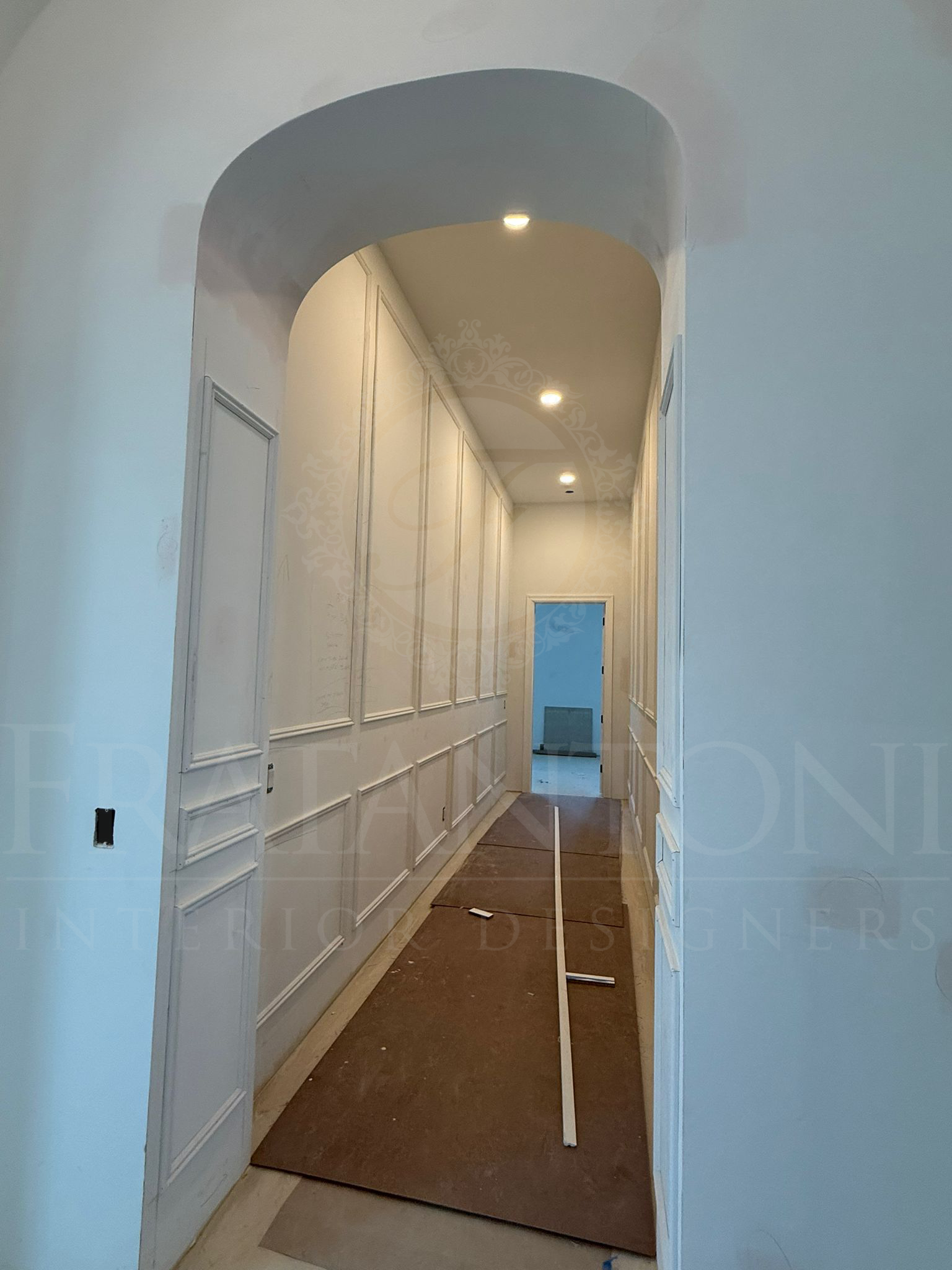 A hallway featuring arched entryways, white walls with decorative molding, and protective paper covering the floor.