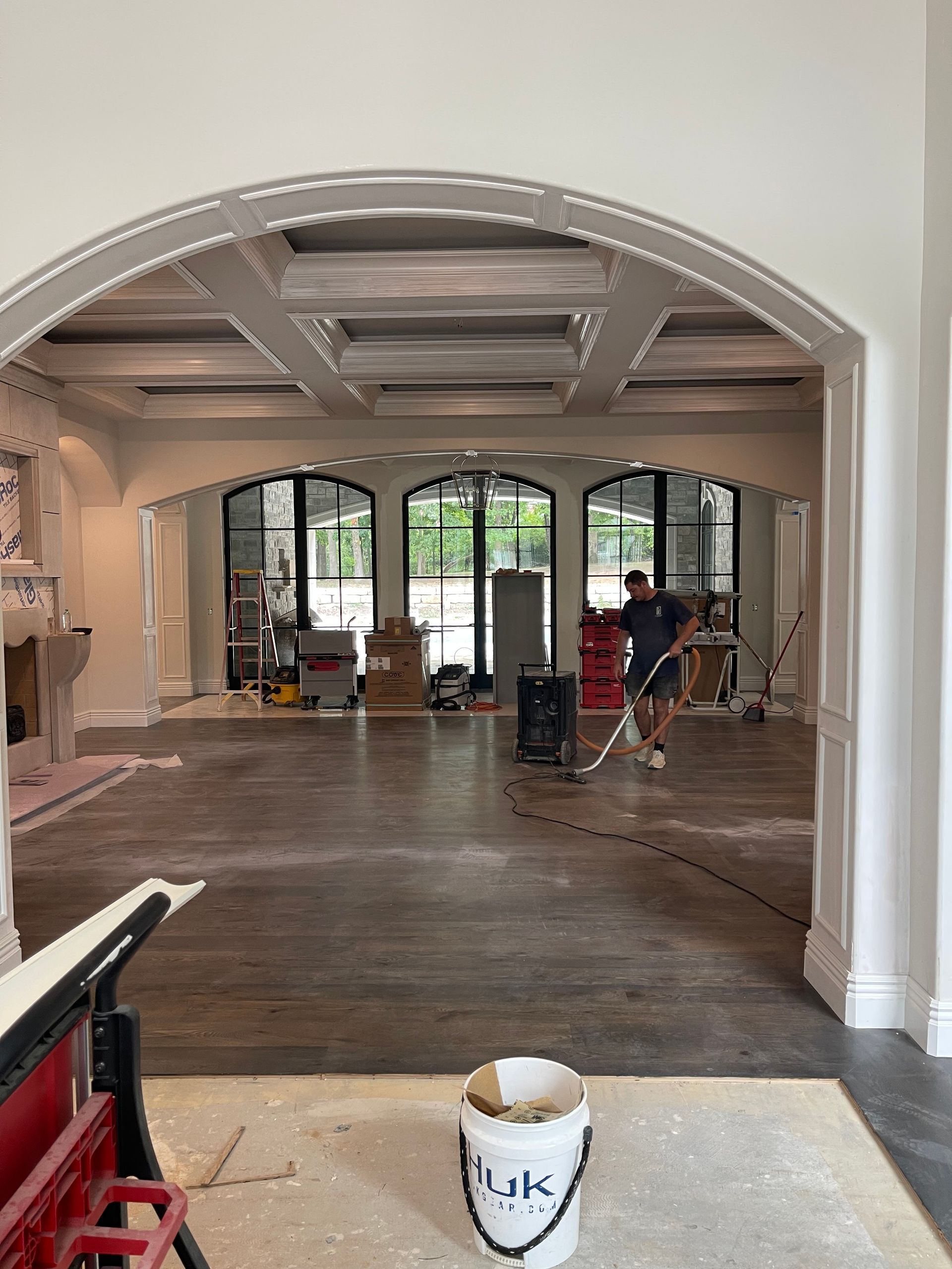 Interior view of a construction site. Man uses a vacuum; arched doorway and coffered ceiling.