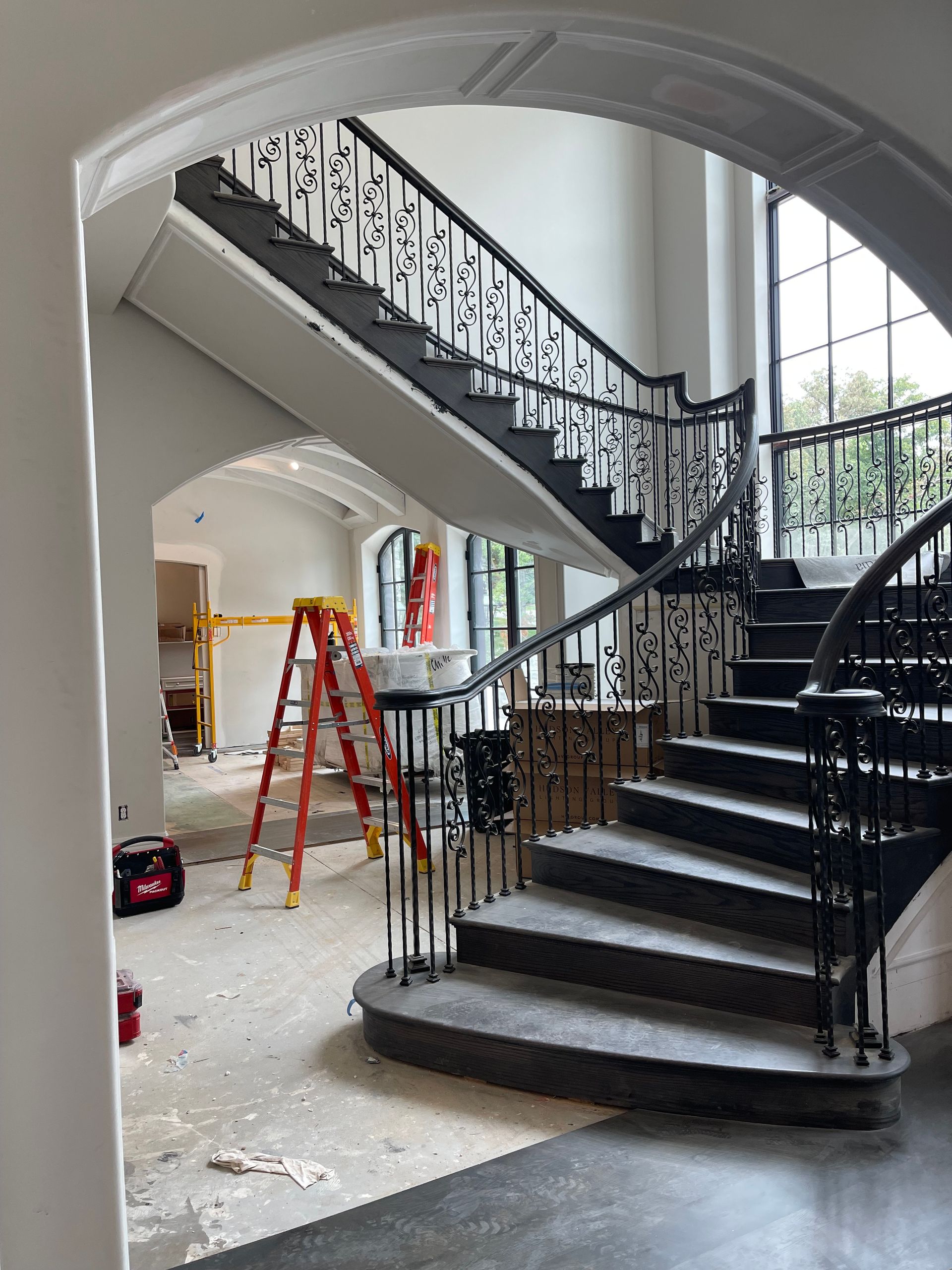 Curved staircase with ornate black railing, under construction, with a ladder and construction tools.