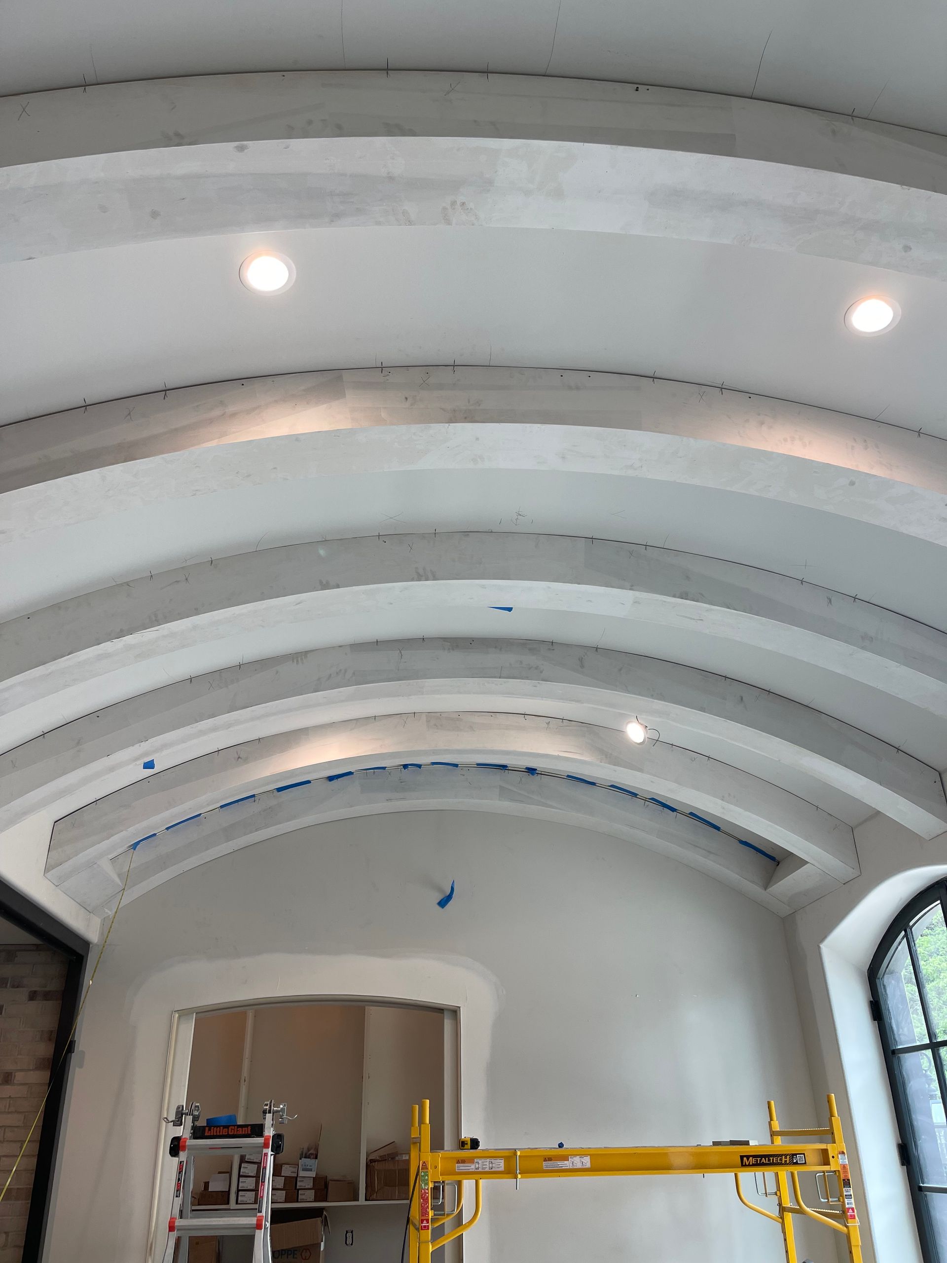 Arched, white ceiling with recessed lighting. A room is under construction, with scaffolding and an open doorway.