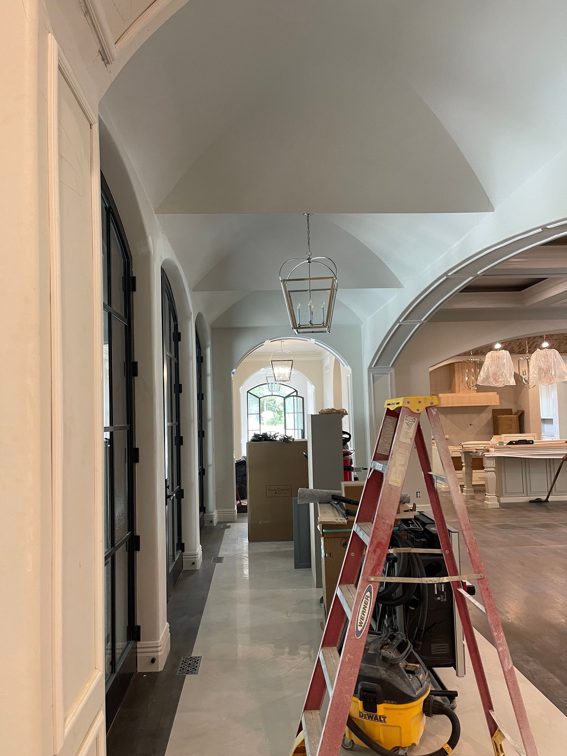 Hallway with arched doorways, ladder, and a hanging light fixture.
