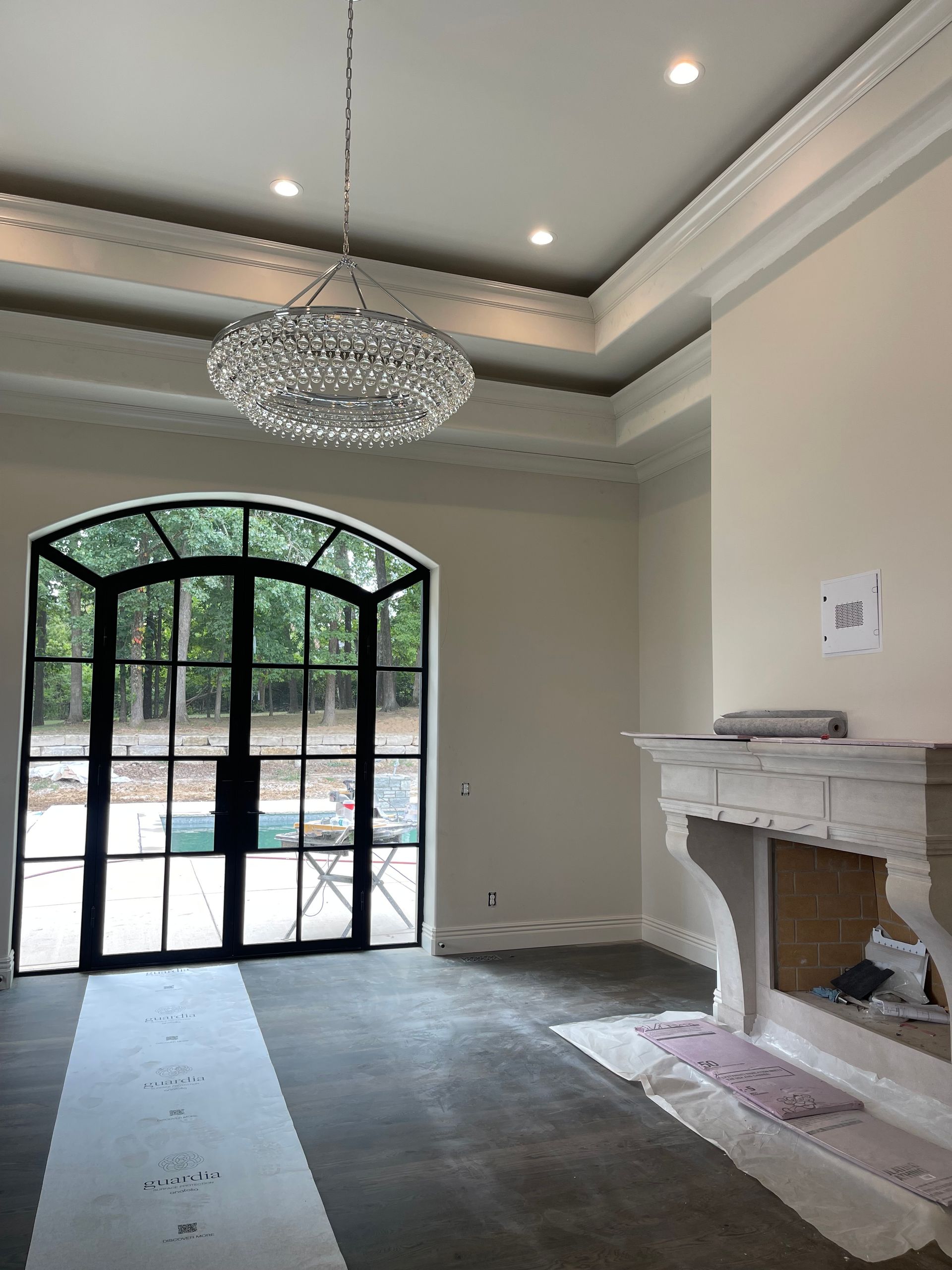 Empty room with large arched black door, fireplace, and chandelier.