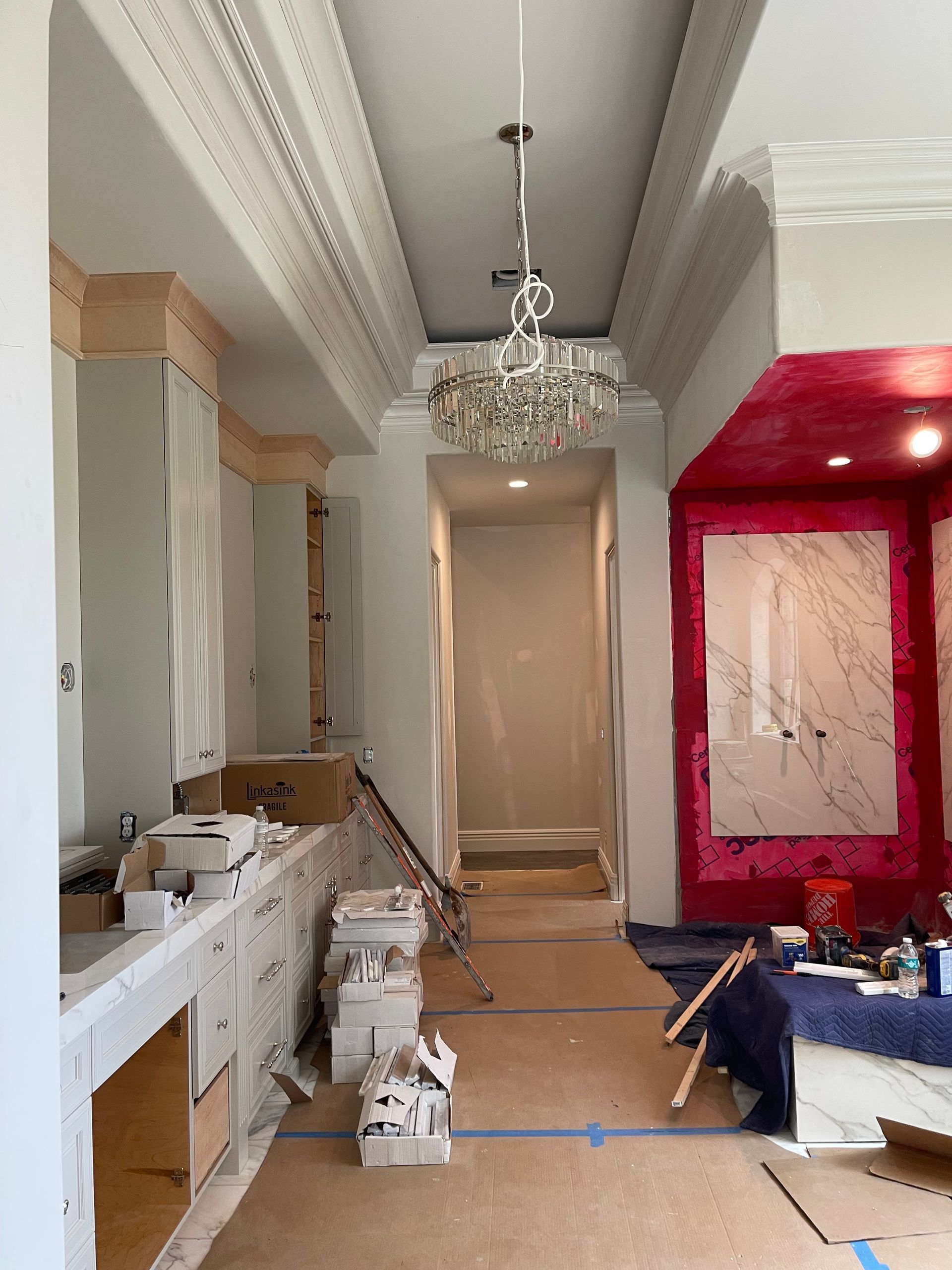 Kitchen under renovation, cabinets and countertop visible. Central hallway leading to an area with red wall.