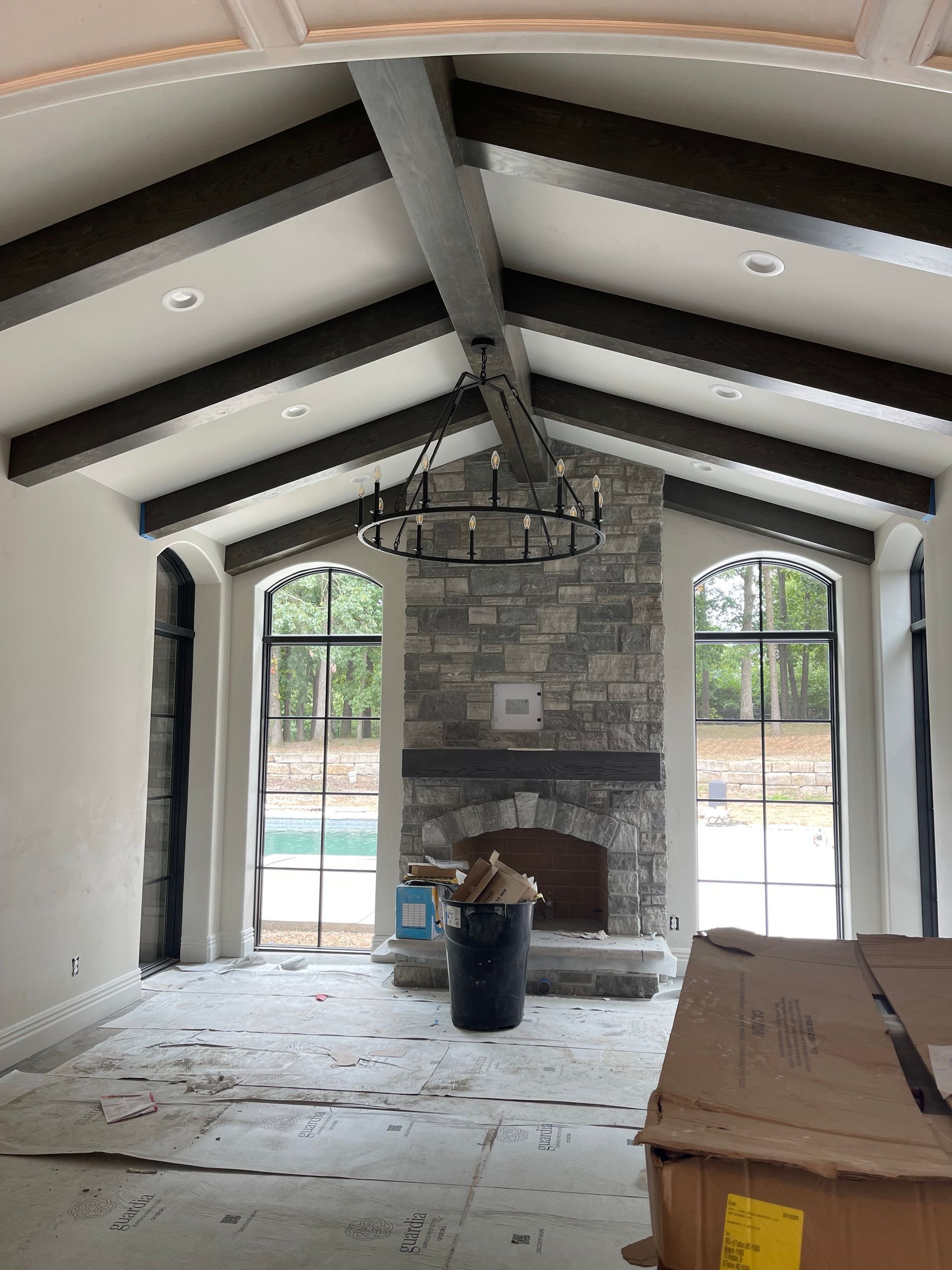 Interior room with stone fireplace, dark beams, large windows, chandelier. Construction debris on the floor.