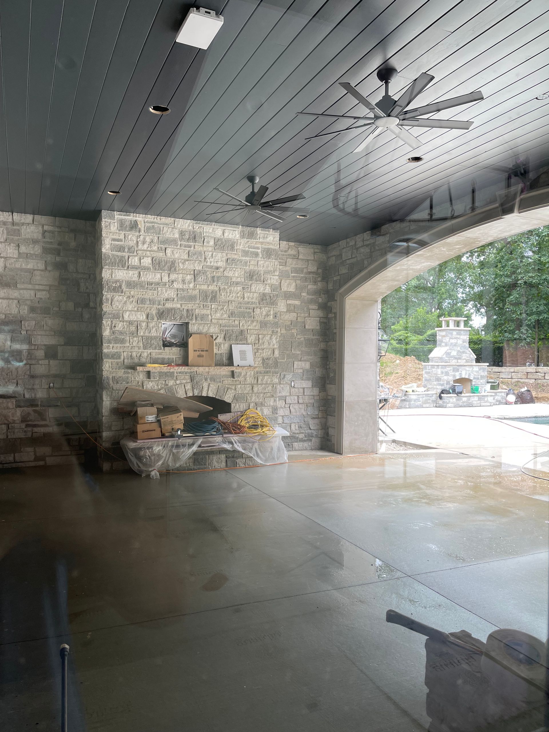 Indoor space with wet concrete floor, stone walls, and arched doorway, ceiling fans.