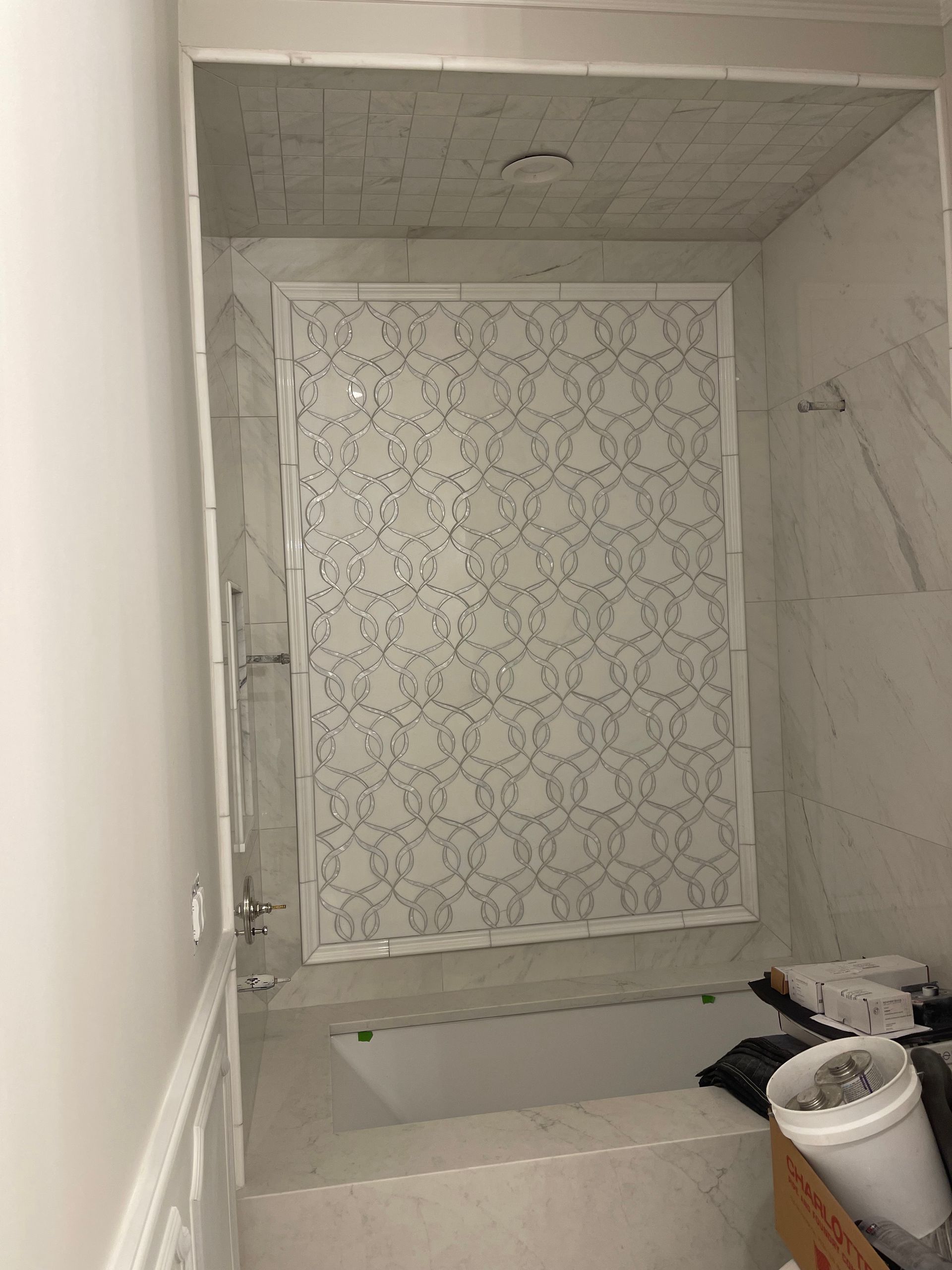 Bathroom with a white tiled shower enclosure. Patterned accent wall, bathtub, and fixtures visible.