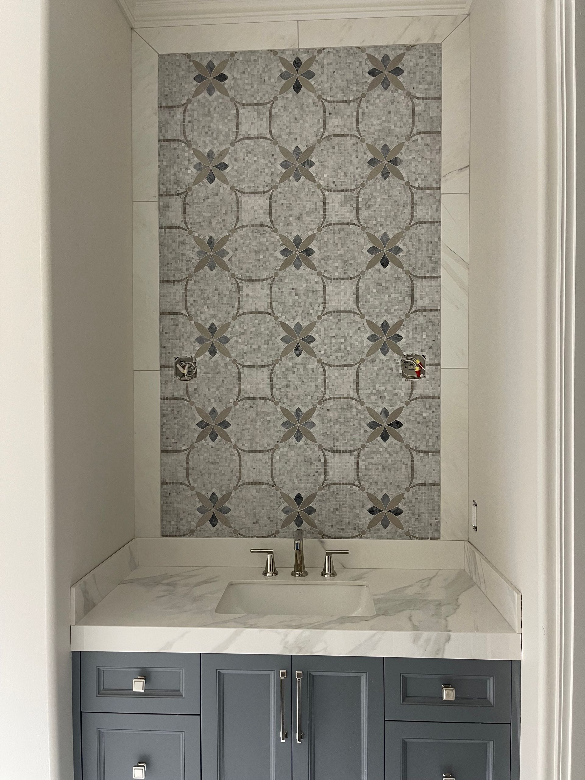 Gray and white patterned tile backsplash above a white countertop, sink, and gray cabinets.