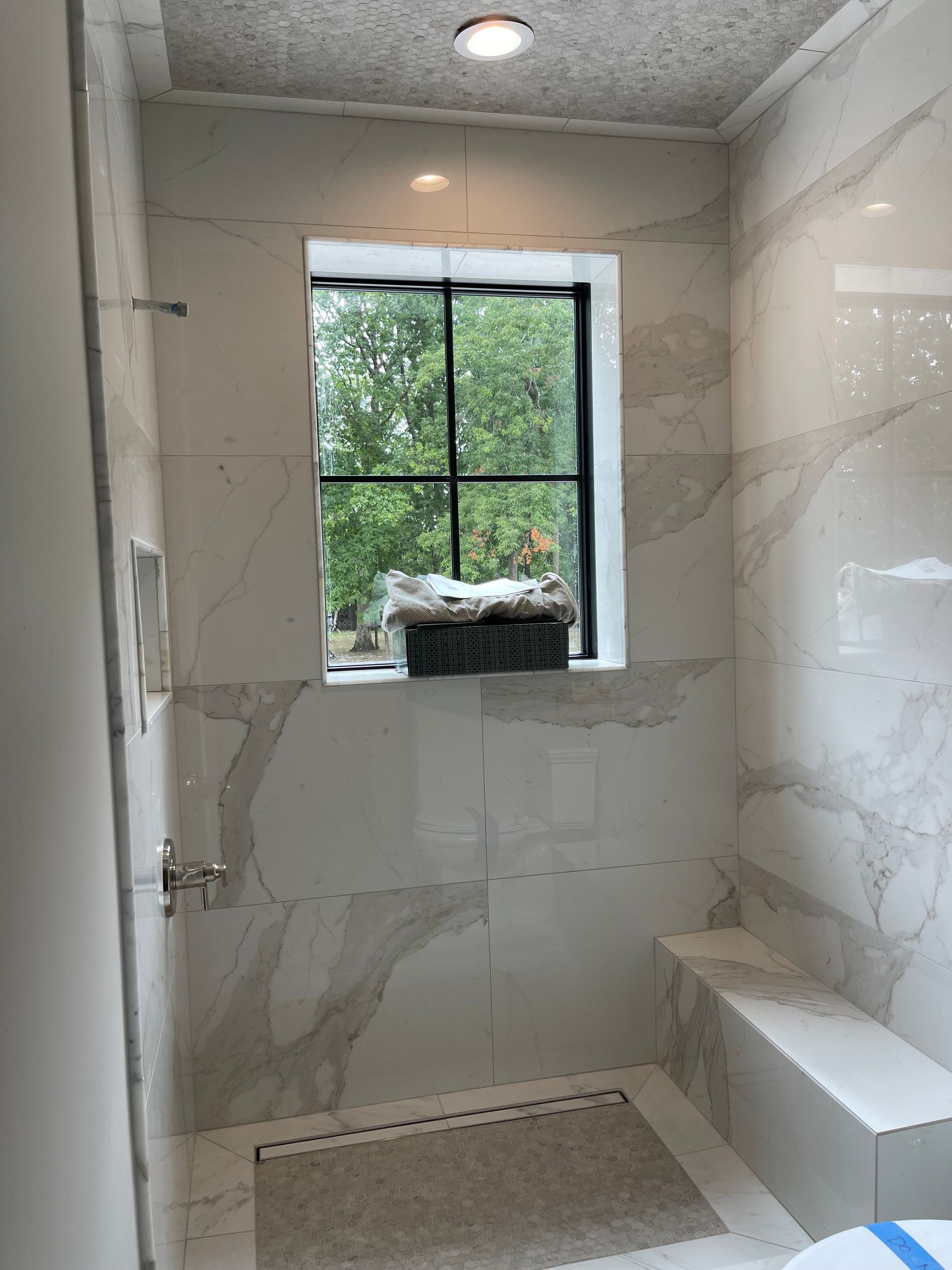 Shower with white marble tile, a window, and a built-in bench.