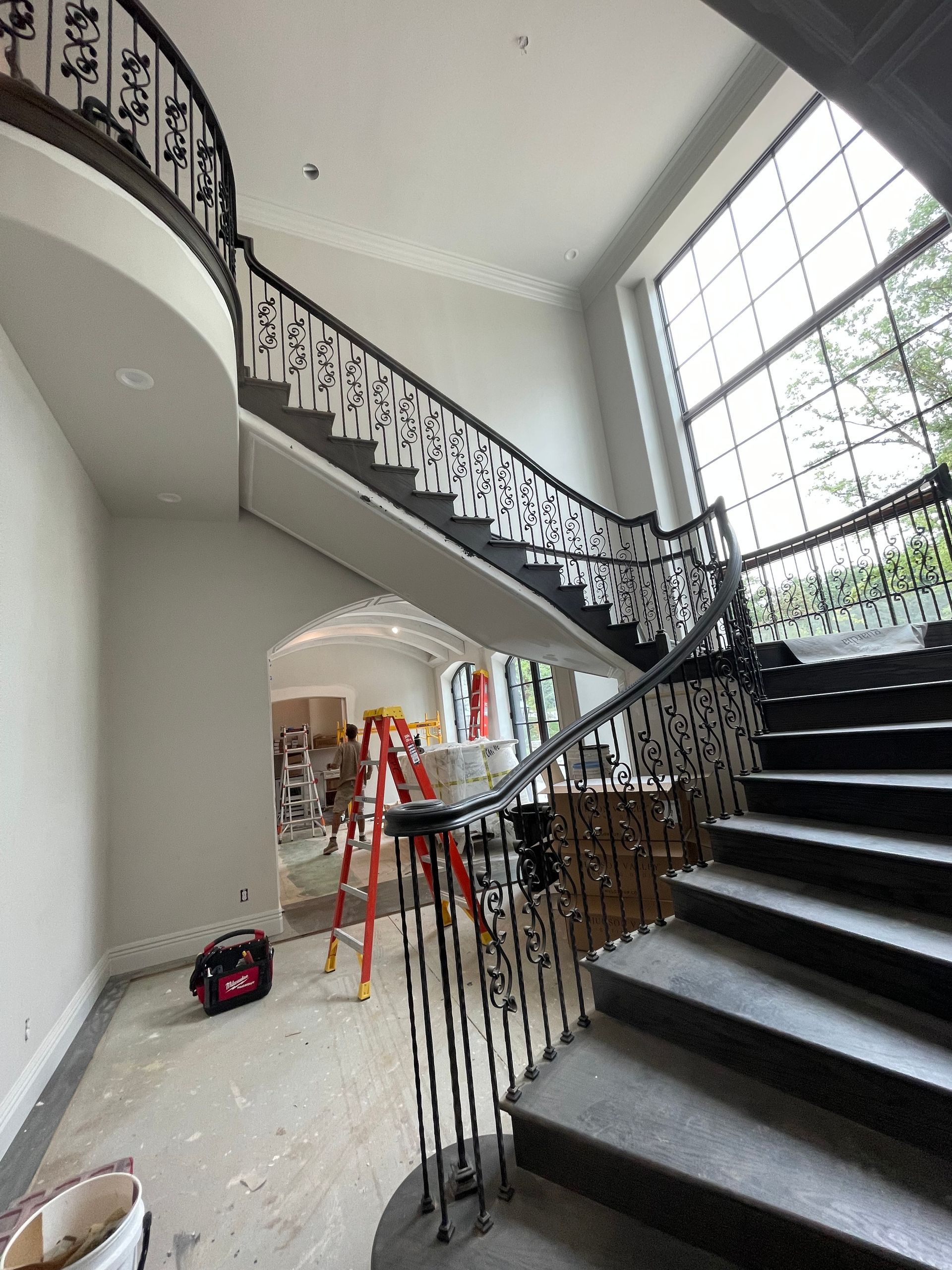 Curving staircase with dark iron railings, gray steps, and a large window. Construction equipment is visible.