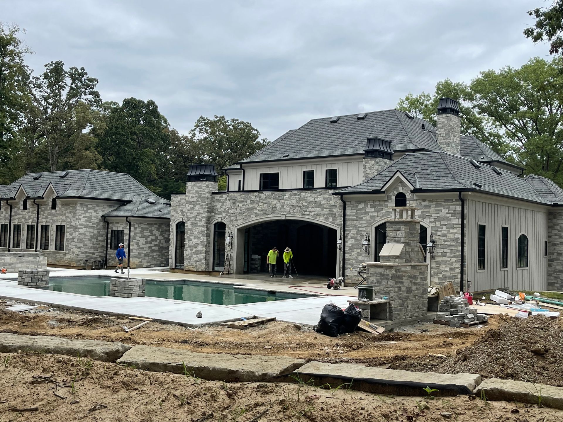 Luxurious house under construction, stone exterior, pool, workers, cloudy sky.