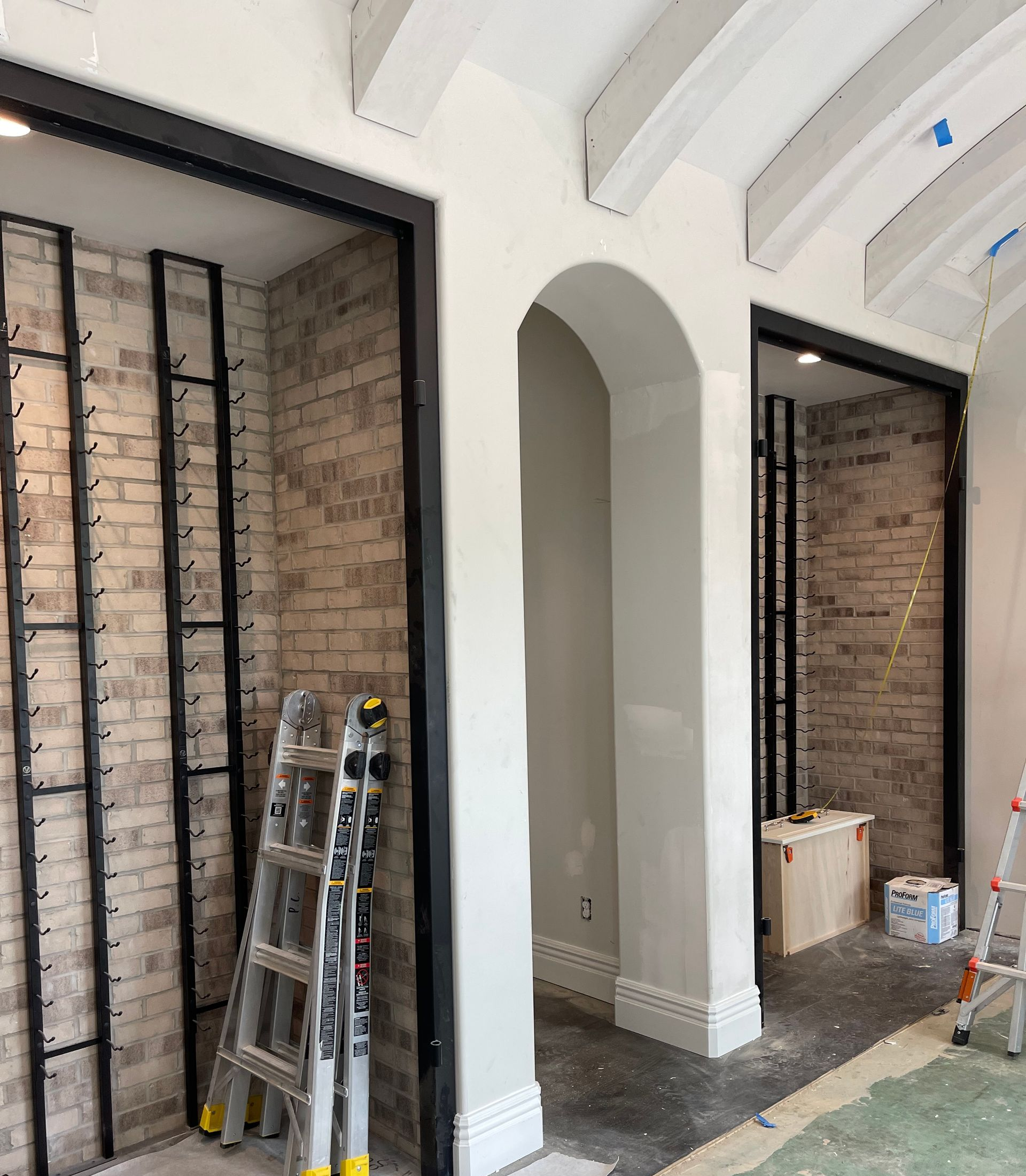 Two archways with brick walls under construction, black frames and ladders present.