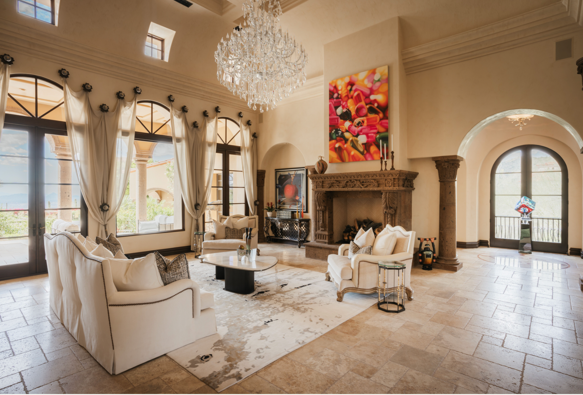 Elegant living room with white furniture, large windows, and a crystal chandelier.