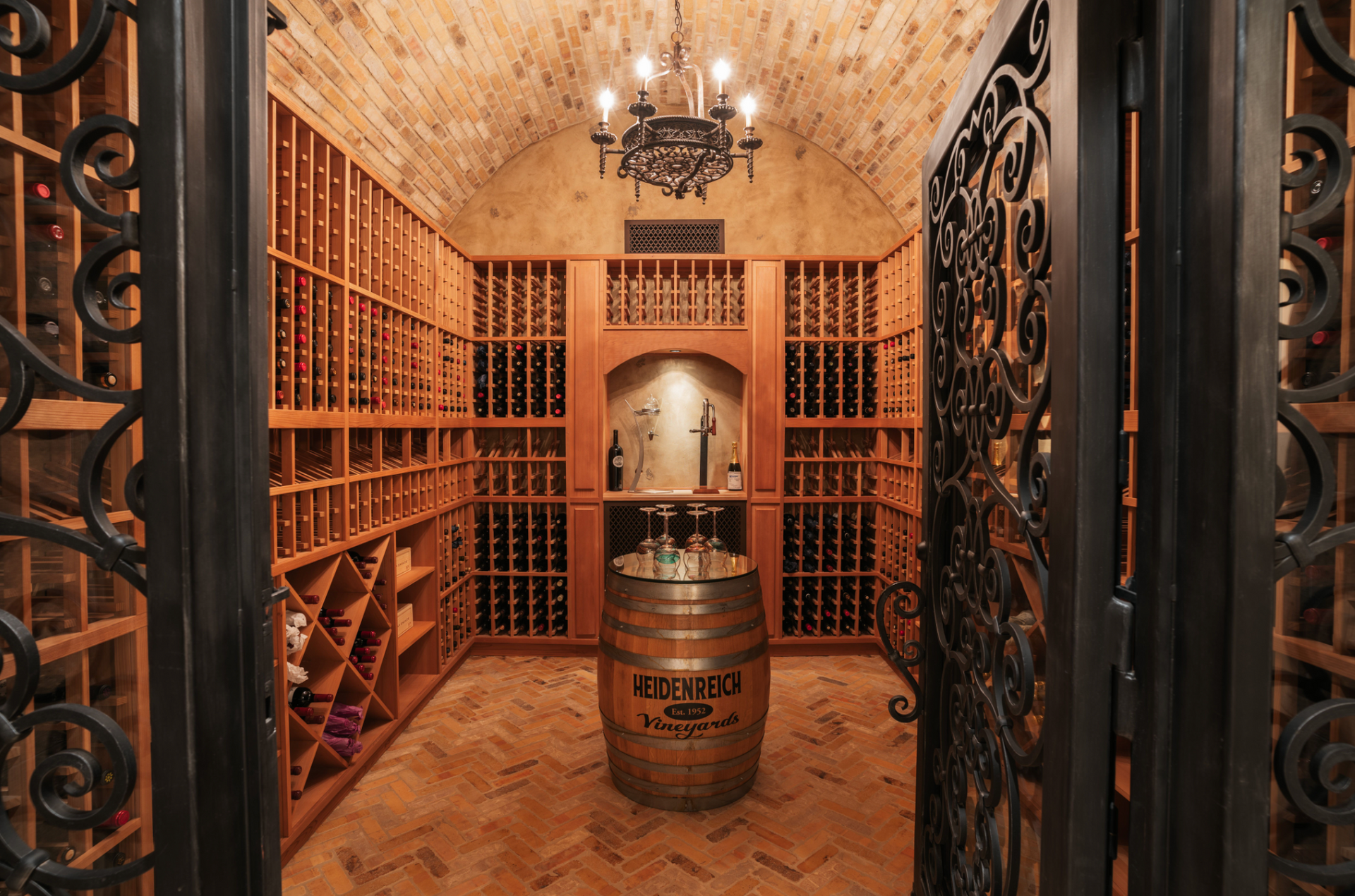 Wine cellar with wood shelving, barrel table, ornate wrought iron door.