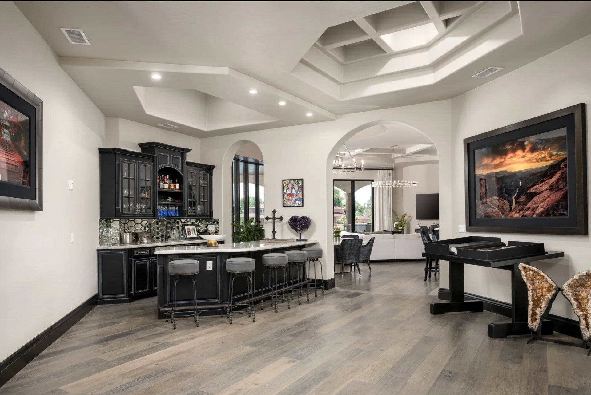 A luxury home interior with a black bar, gray stools, and artwork on white walls.