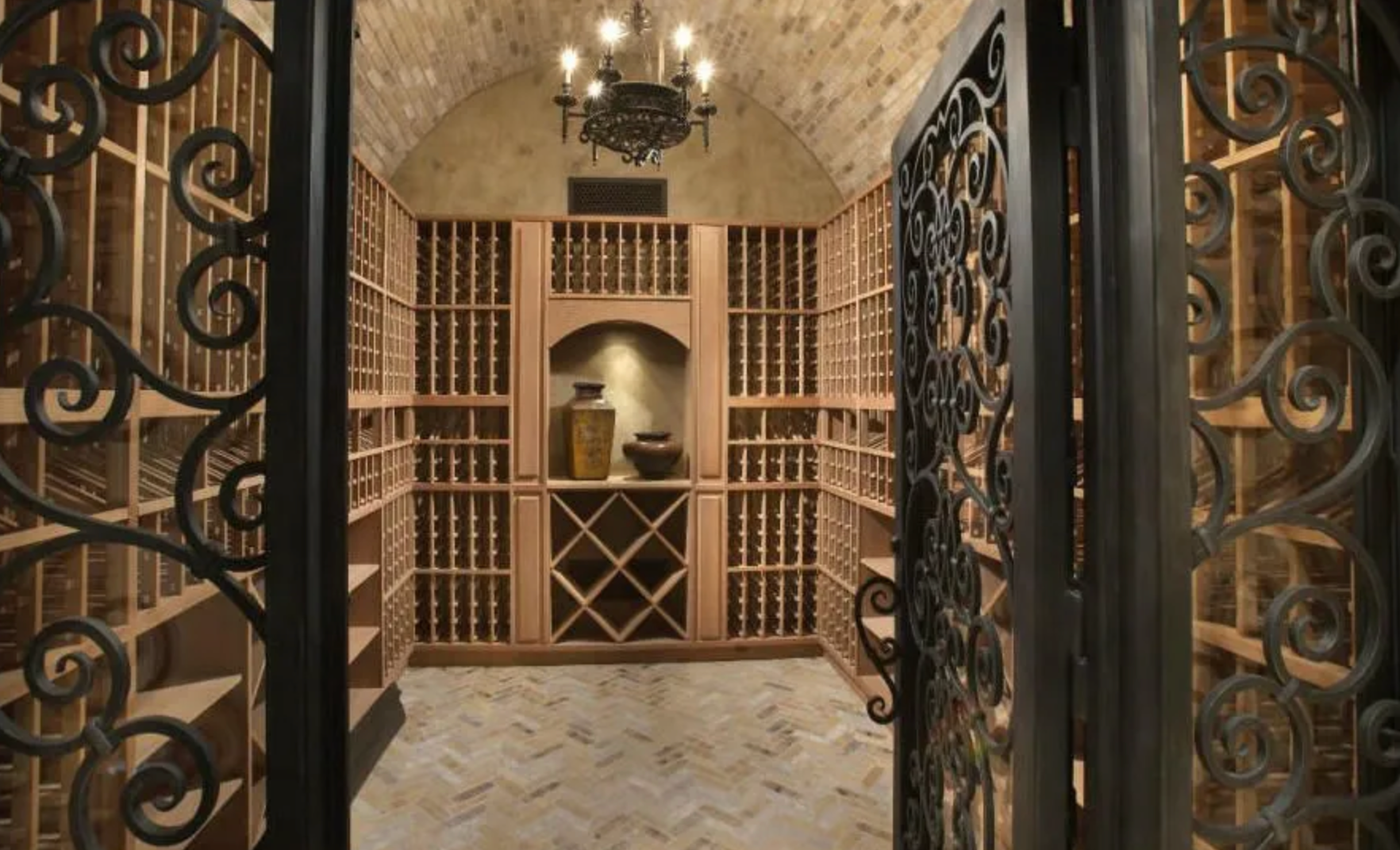 Wine cellar with wooden racks, wrought-iron gate, and arched brick ceiling.