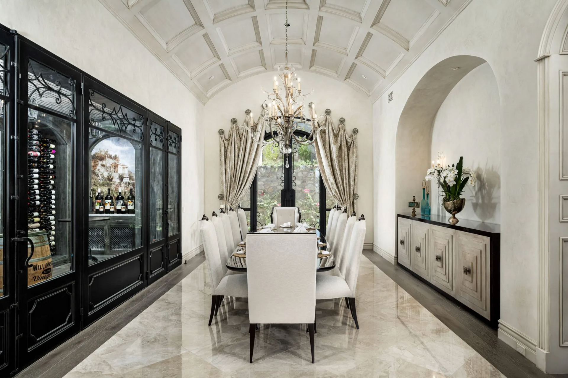 Elegant dining room with arched ceiling, chandelier, long table set for a meal, and decorative cabinets.