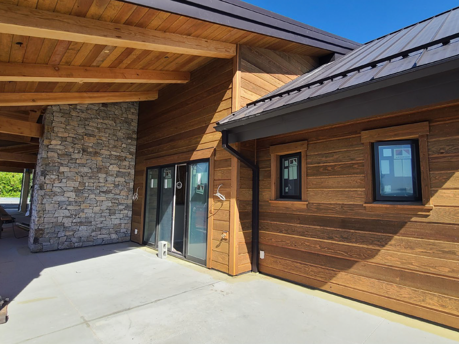 Exterior of a modern home with brown siding, dark windows, and a stone pillar.