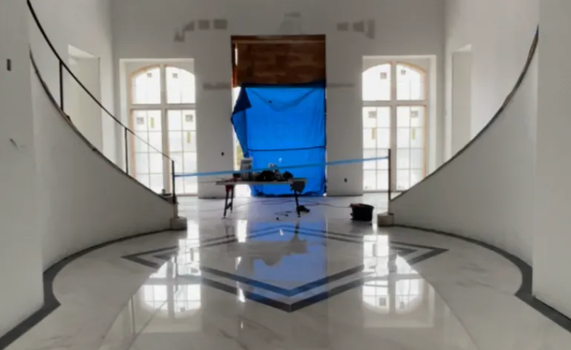 Grand foyer with marble floor, arched windows, and curved staircases; construction in doorway.
