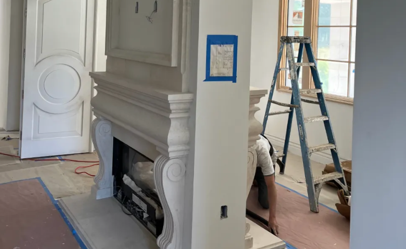 Fireplace with decorative molding, open door, ladder, and a person working in a room under construction.