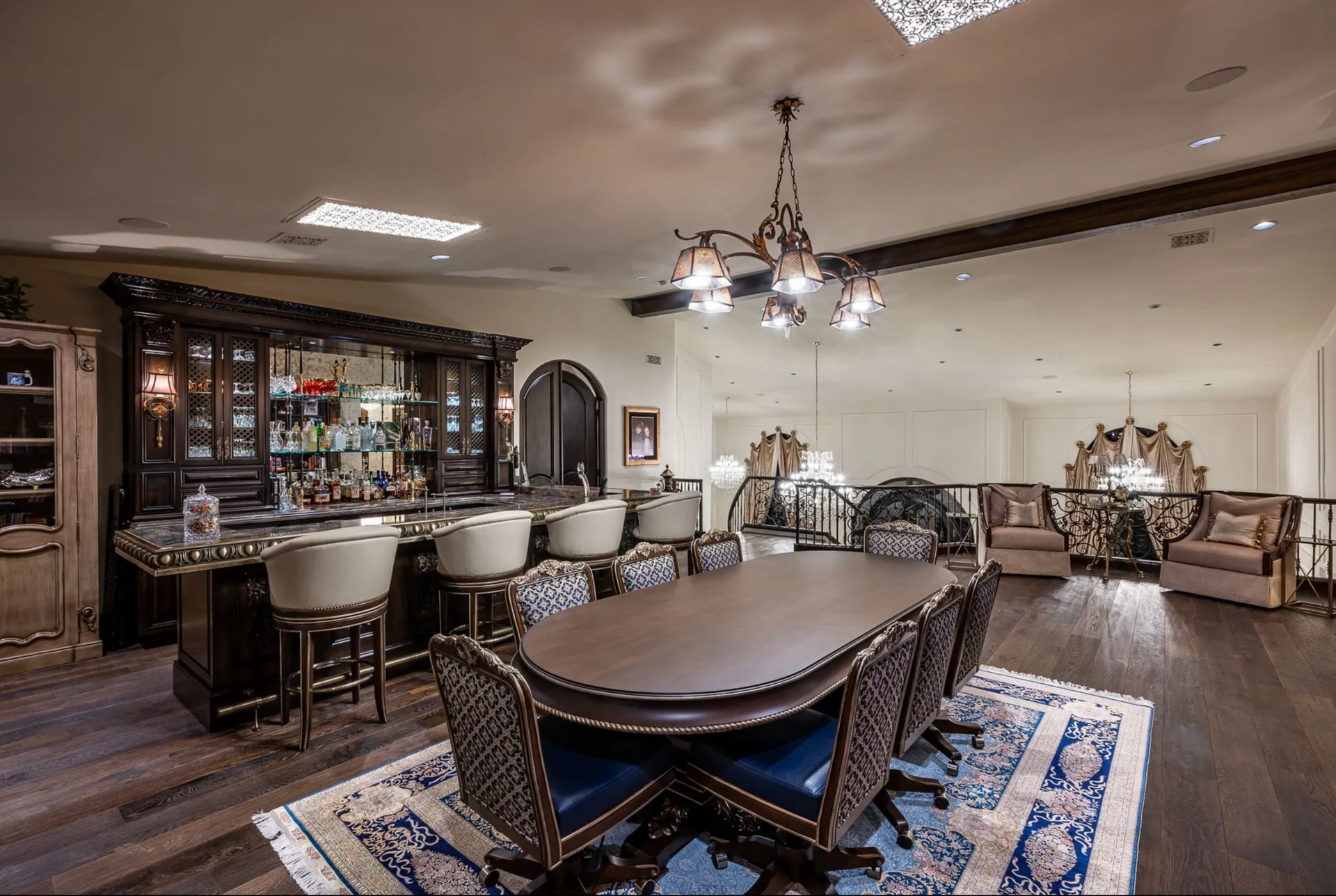 Luxurious room with bar, table, chairs, and ornate chandelier. Dark wood and blue accents.
