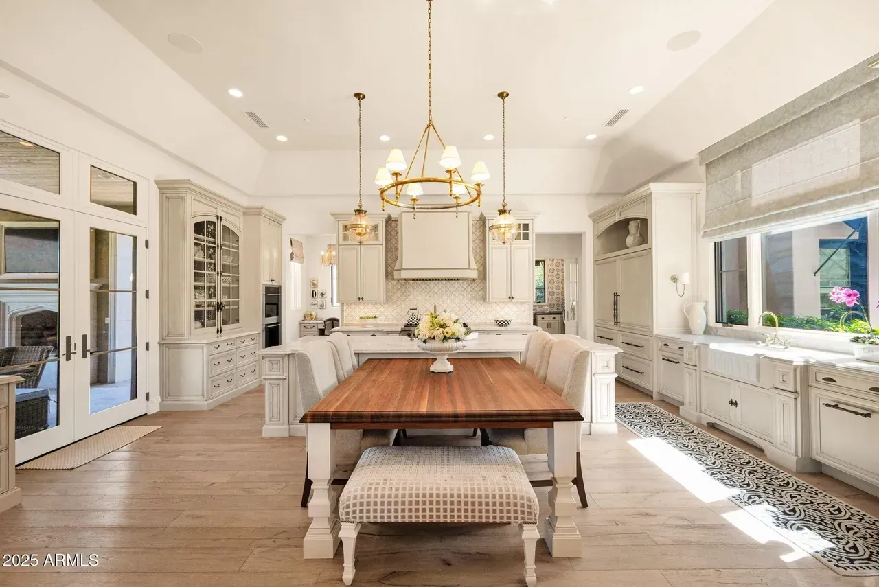 Spacious white kitchen with wood table, gold chandelier, and patterned floor runner.