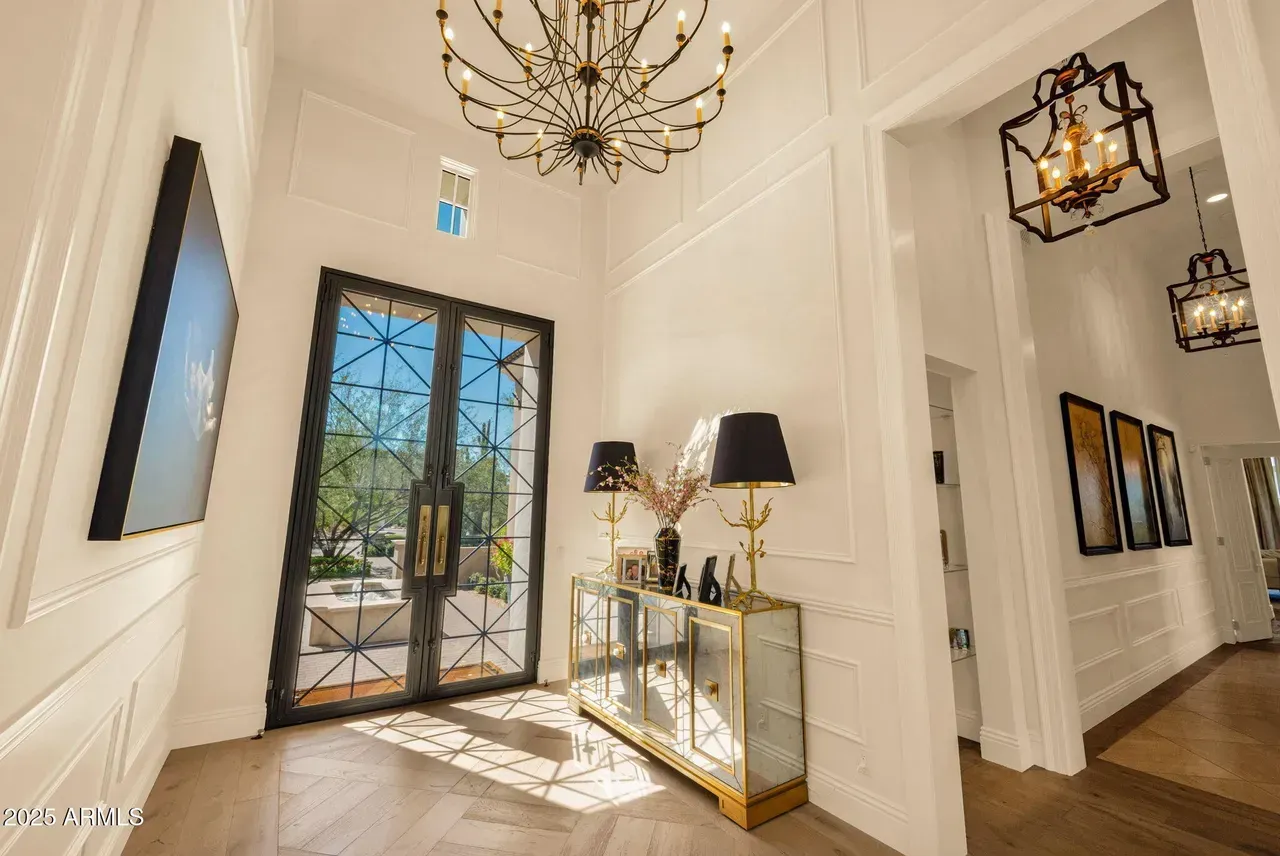 Elegant foyer with gold chandelier, mirrored console, and geometric glass doors.