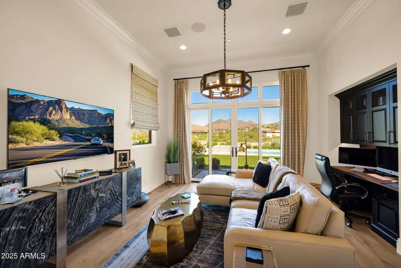 Living room with large windows, leather sofa, TV, desk, and mountain view.