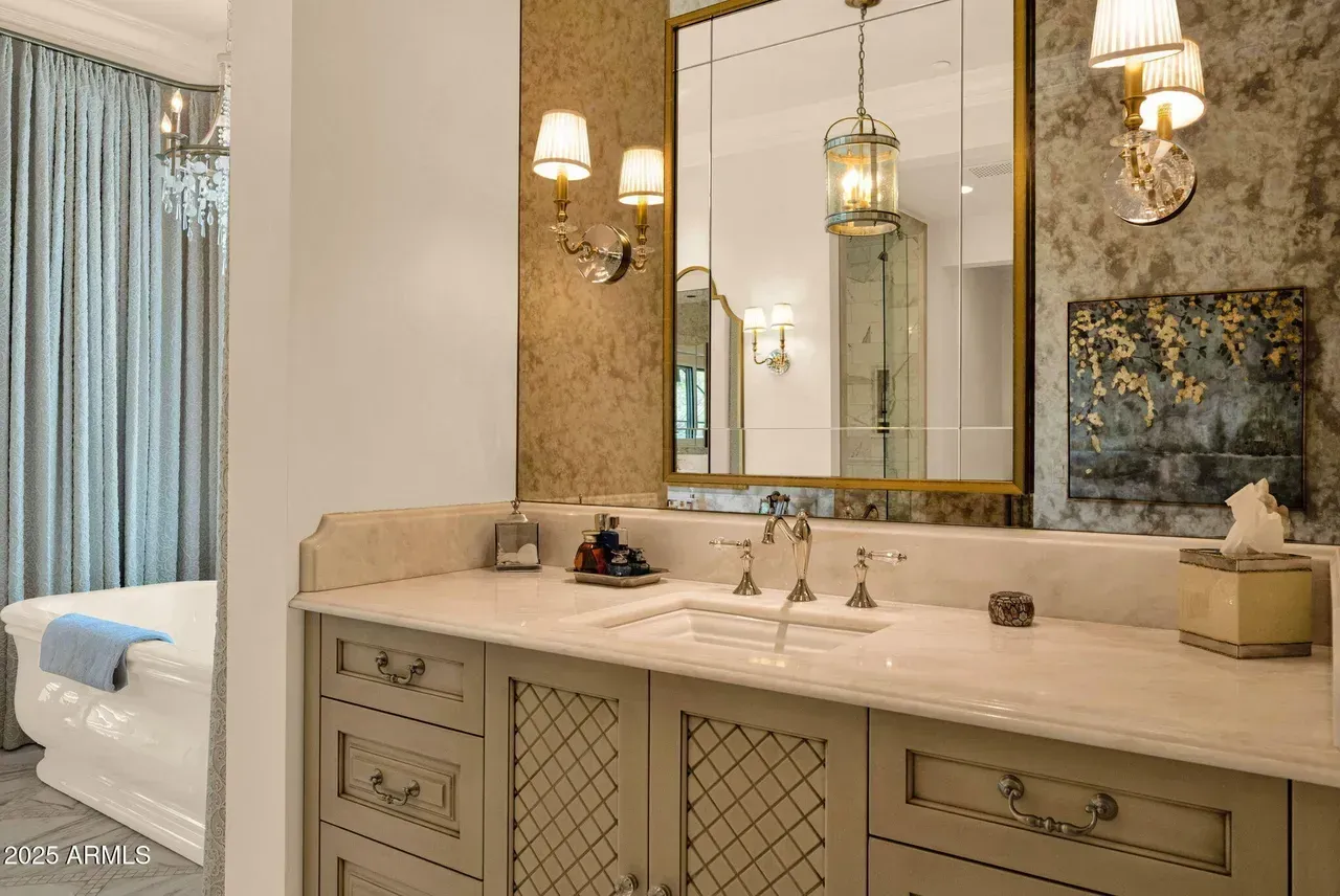 Elegant bathroom with marble countertop, ornate mirror, sconces, and light blue curtains.
