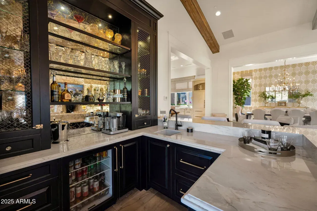 Dark wood home bar with mirrored shelves, marble countertops, and a dining area visible beyond.