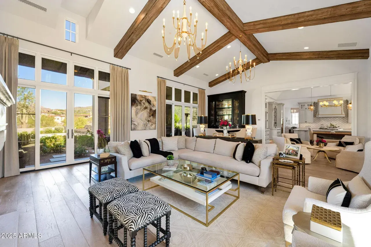Elegant living room with white walls, exposed wooden beams, large windows, and cream-colored furniture.