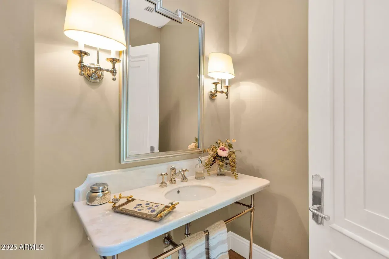 A small, elegant bathroom with a white marble vanity, chrome fixtures, and sconce lighting.
