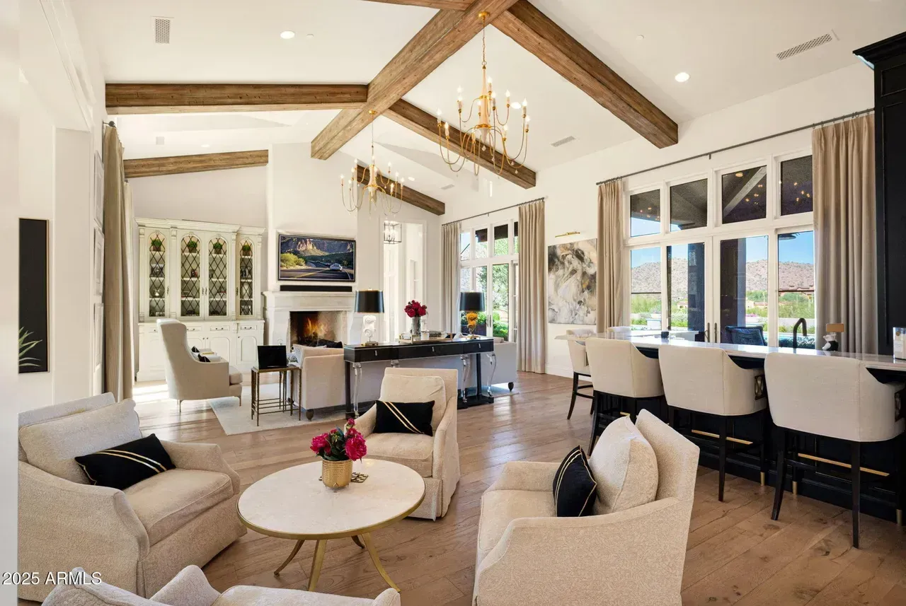 Spacious living room with wood beams, fireplace, and bar seating; neutral tones and natural light.