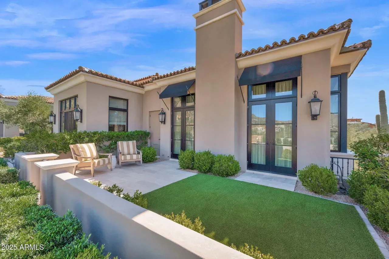 Exterior of a modern house with a patio, lawn, and mountain view, on a sunny day.
