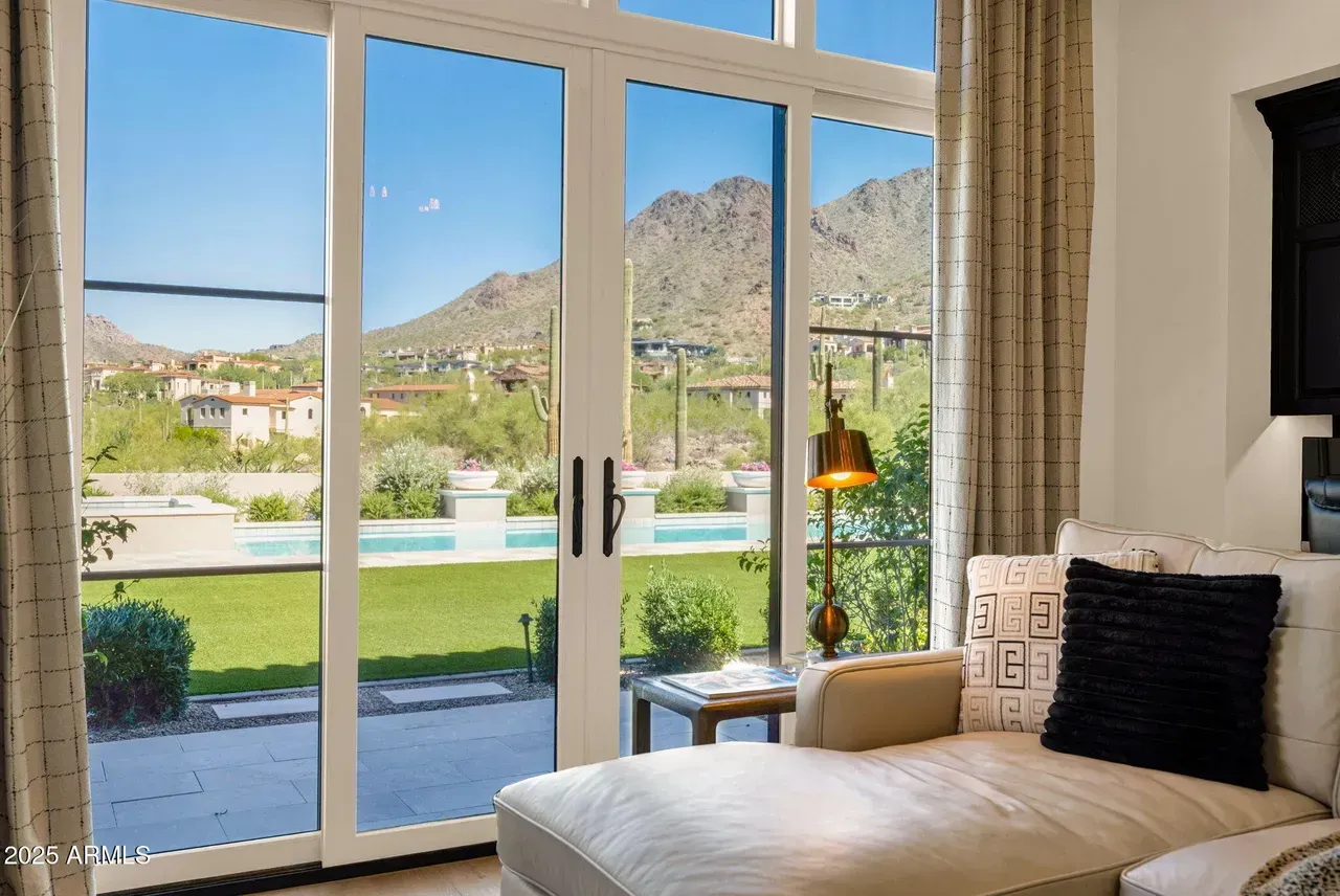 A bright room with a chaise lounge and a large window overlooking a pool, greenery, and mountains.