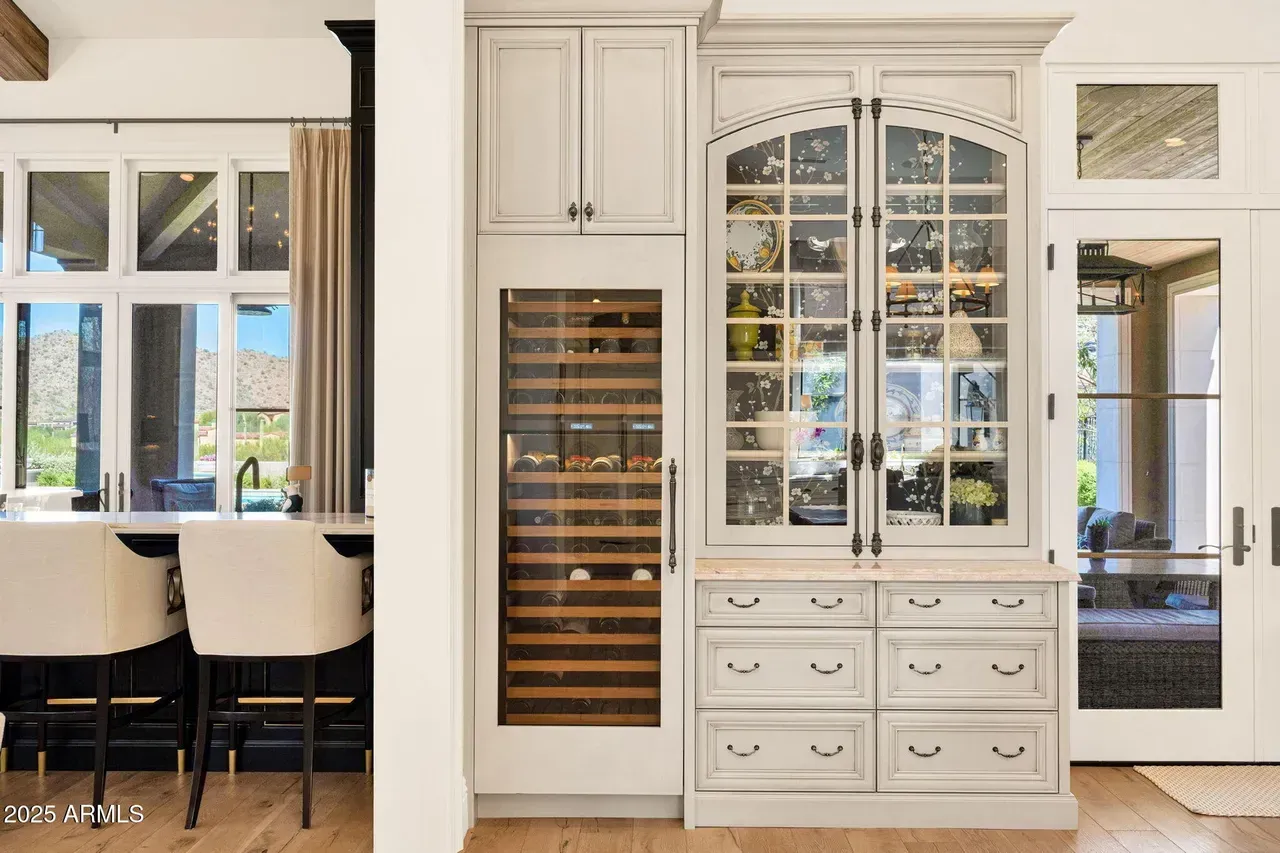 Kitchen wine storage cabinet with a wine fridge and display shelves, light gray cabinets, and light wood flooring.
