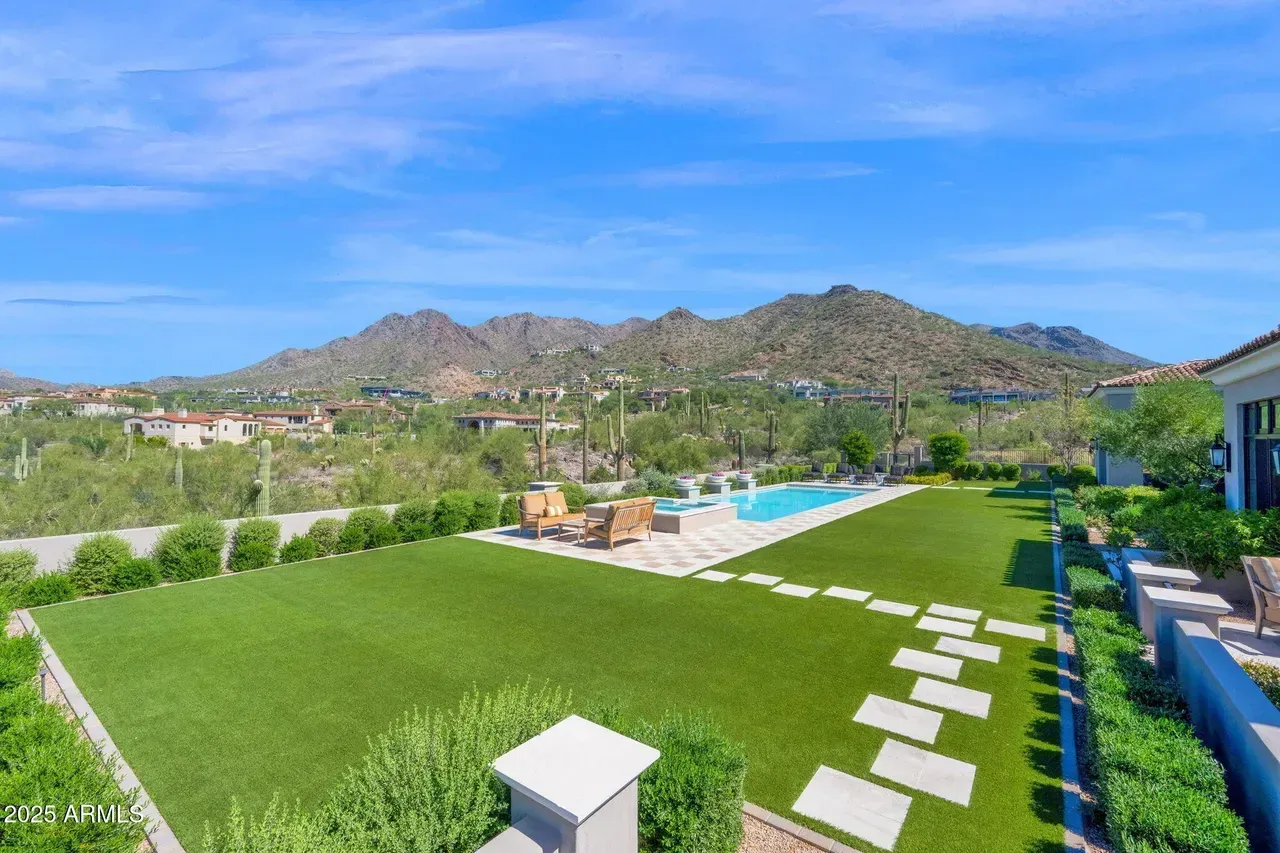 Lush green lawn with pool, stone walkway, lounge chairs, and mountain backdrop under blue sky.