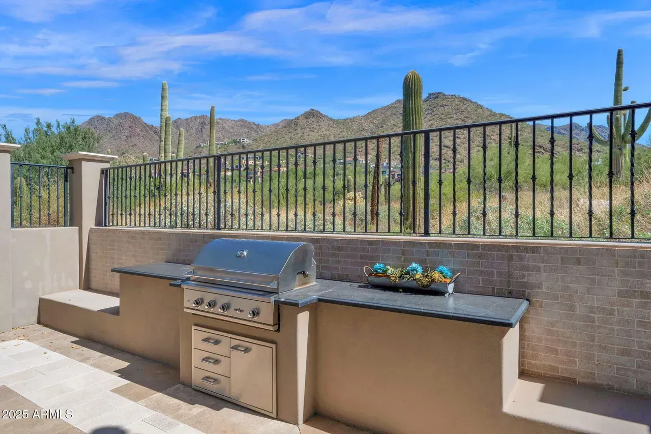Outdoor kitchen with grill, countertops, and a view of mountains and cacti under a blue sky.