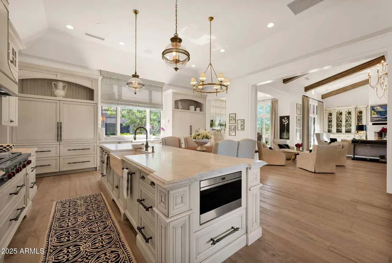 Luxurious white kitchen with island, pendant lights, and view into the living room.