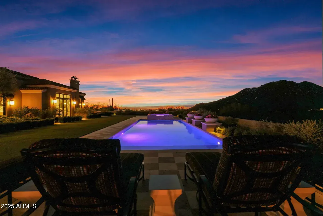 Two lounge chairs face a pool and sunset over distant mountains.