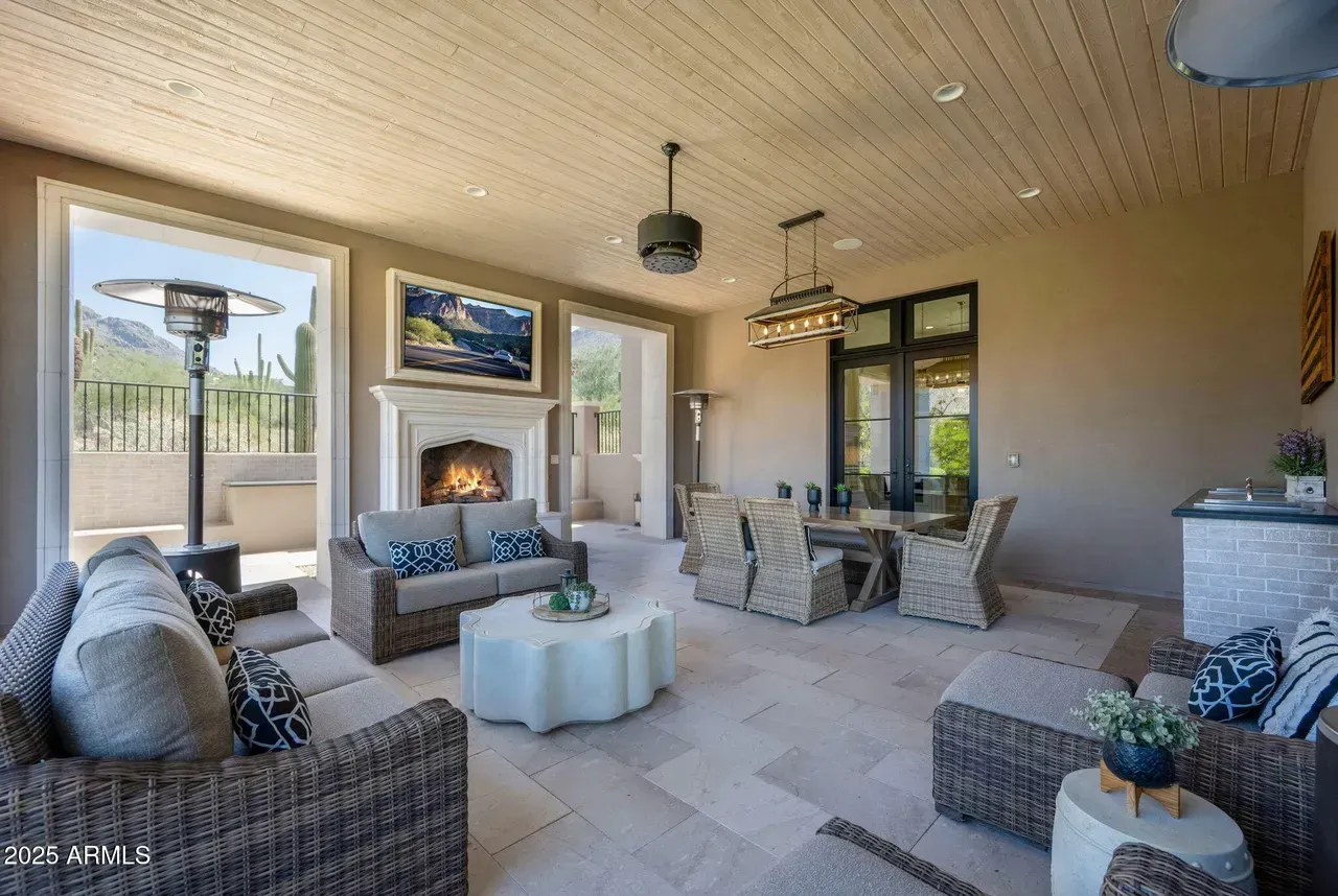 Covered outdoor living space with furniture, fireplace, and dining table.