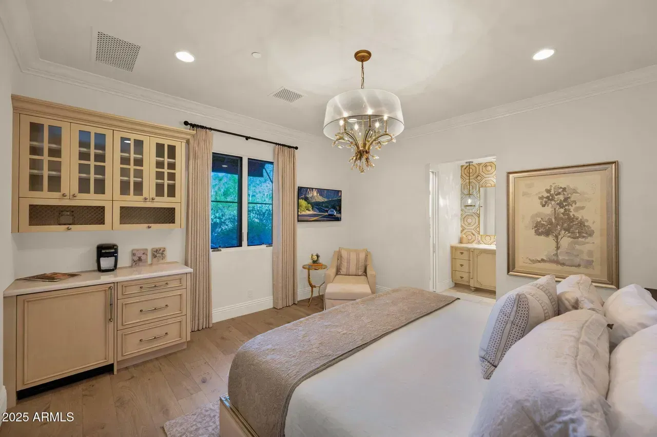 Elegant bedroom with light-toned cabinetry, a chandelier, and a view through a window.