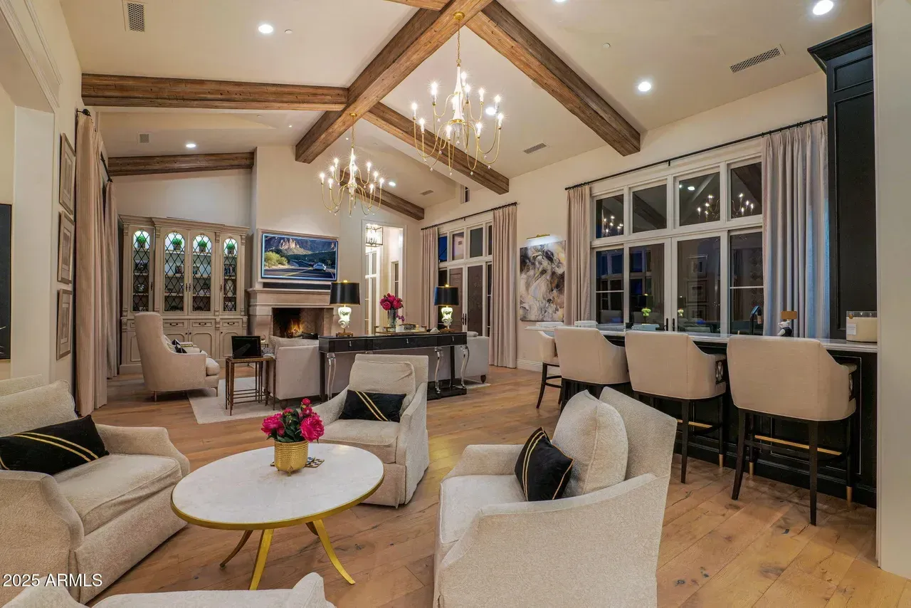 Living room with high ceilings, exposed beams, fireplace, and a bar with stools.