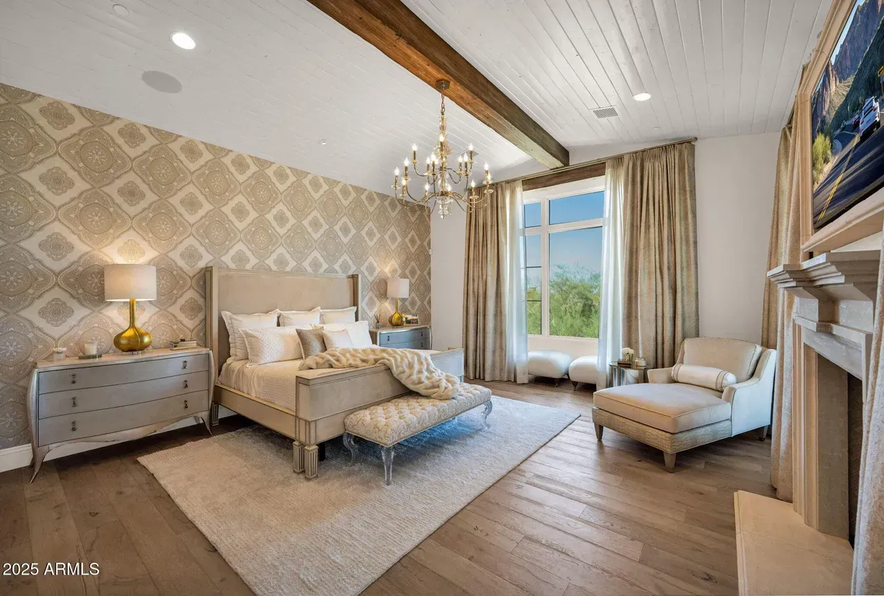 Elegant bedroom with gold and cream tones, large window, and chandelier.