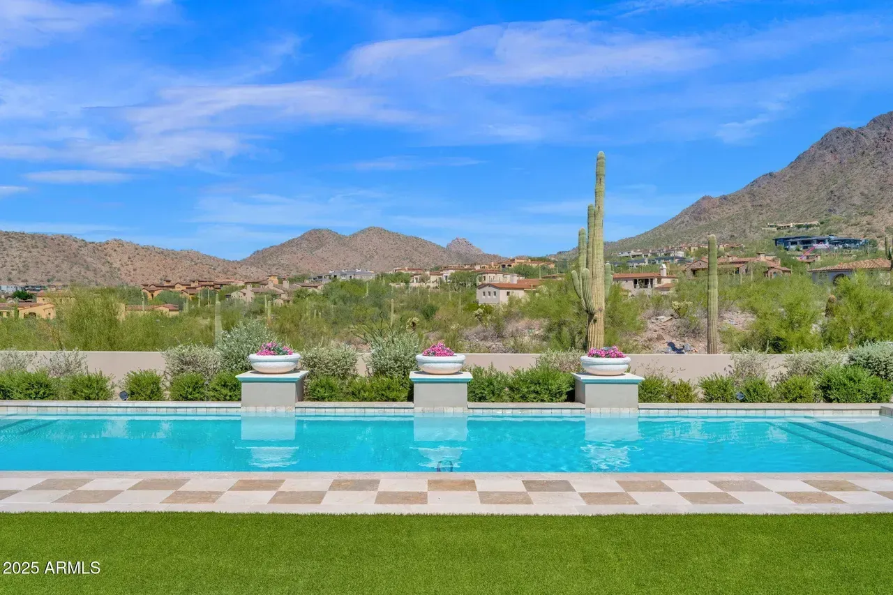 Swimming pool with mountain view, surrounded by desert landscaping and green lawn under a blue sky.