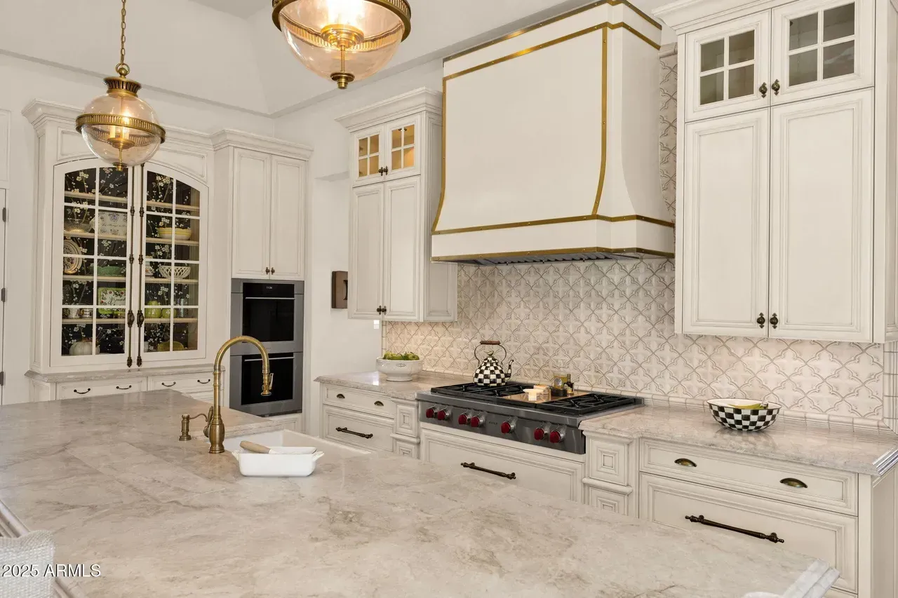 Elegant white kitchen with marble countertops, gold accents, and a large window.