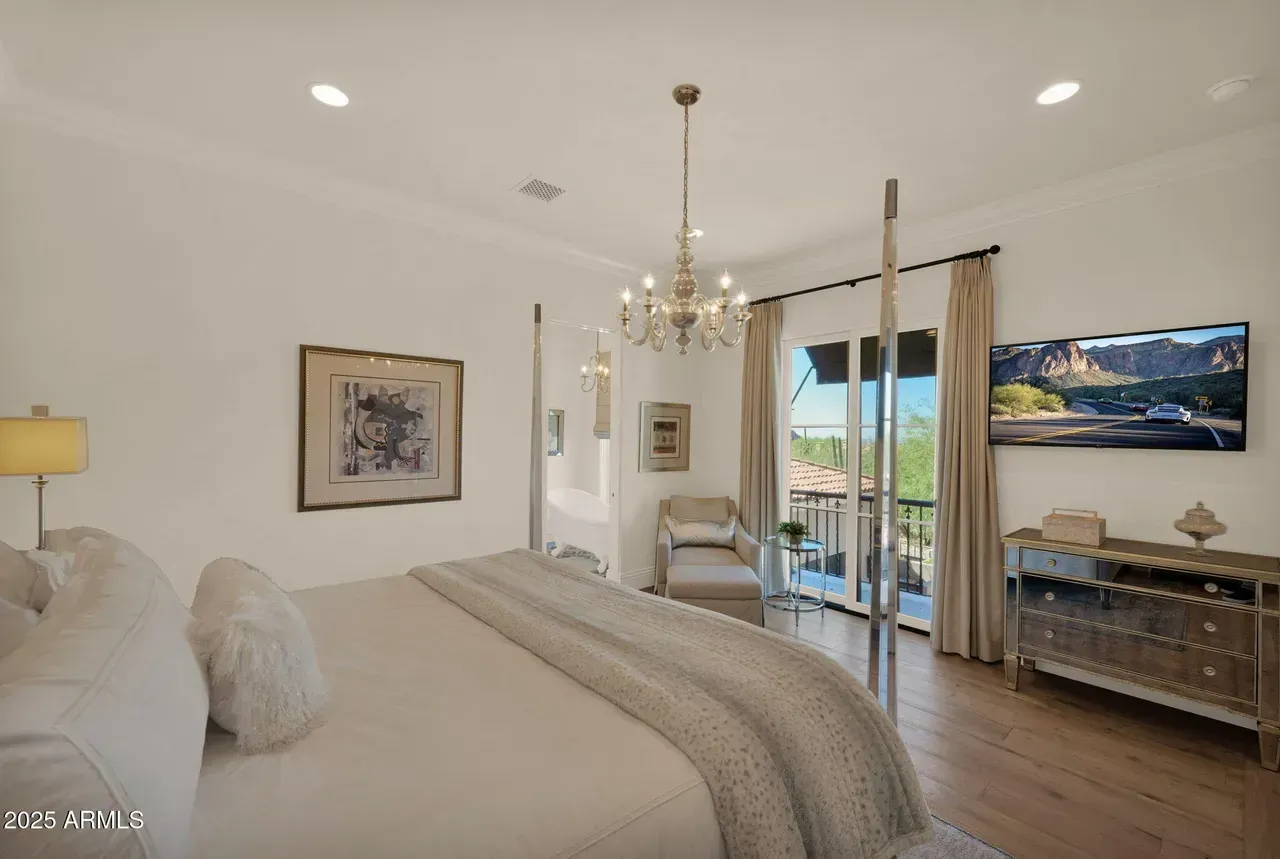 Bedroom with bed, chandelier, balcony access, neutral colors.